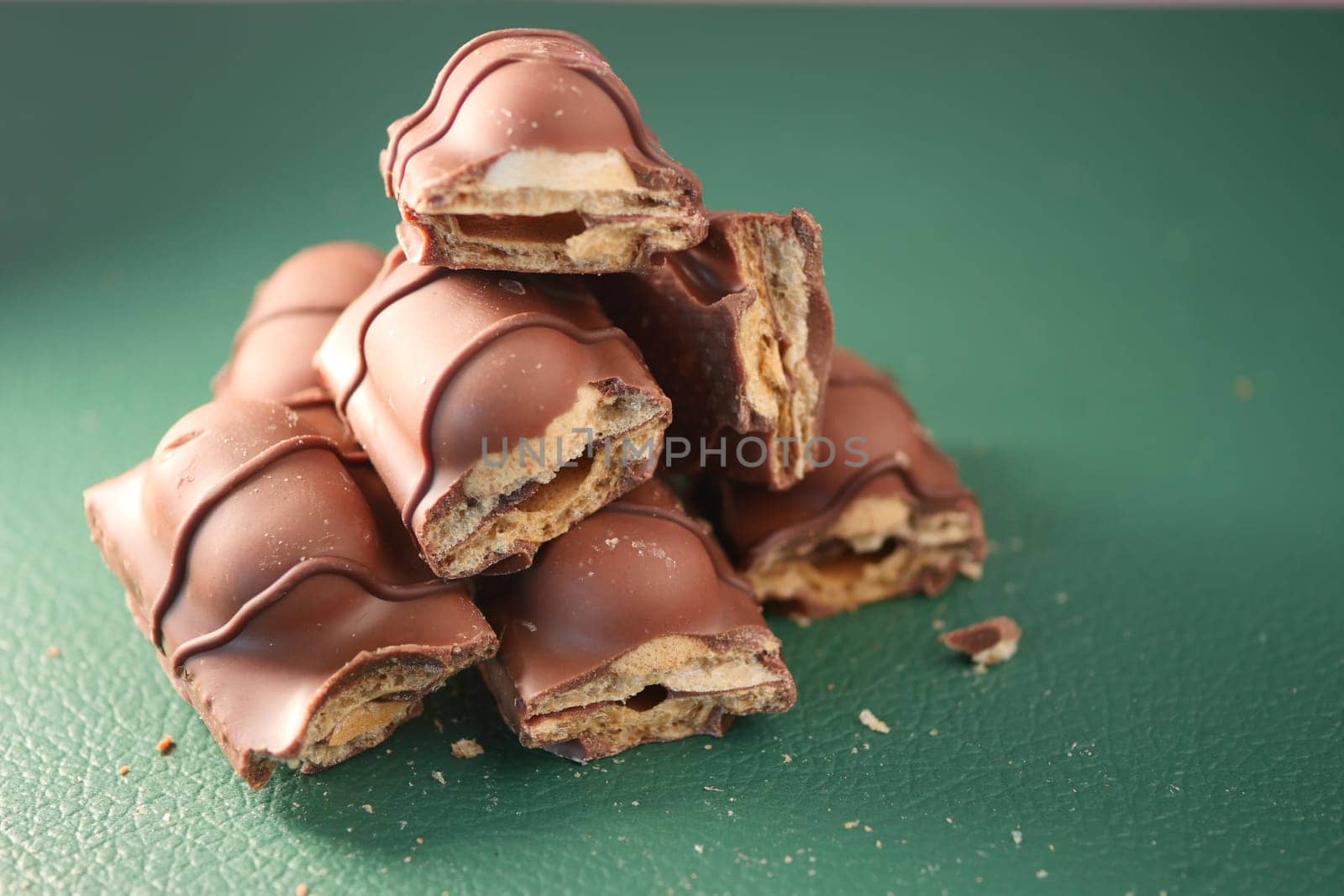 Chocolate-covered snack bars are stacked artfully on a green surface.