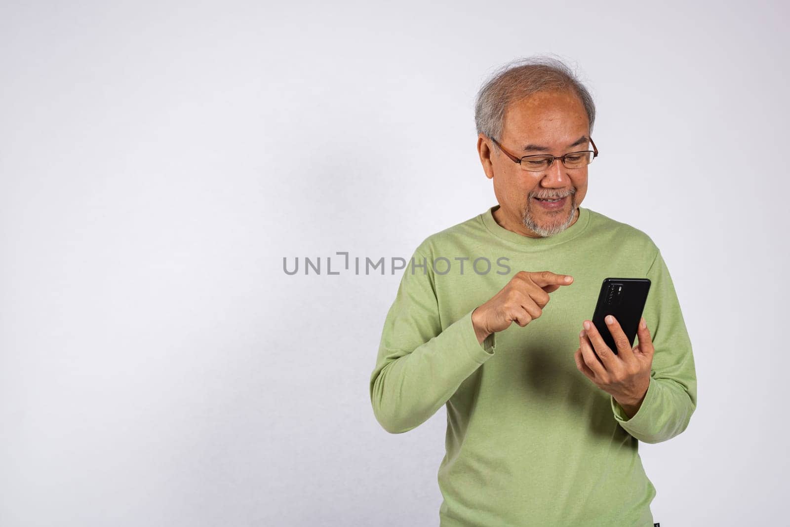 Portrait smiling Asian older man smiling and pointing at his cell phone studio shot isolated on white background. elderly holding mobile phone in hand. Concept of connection and communication