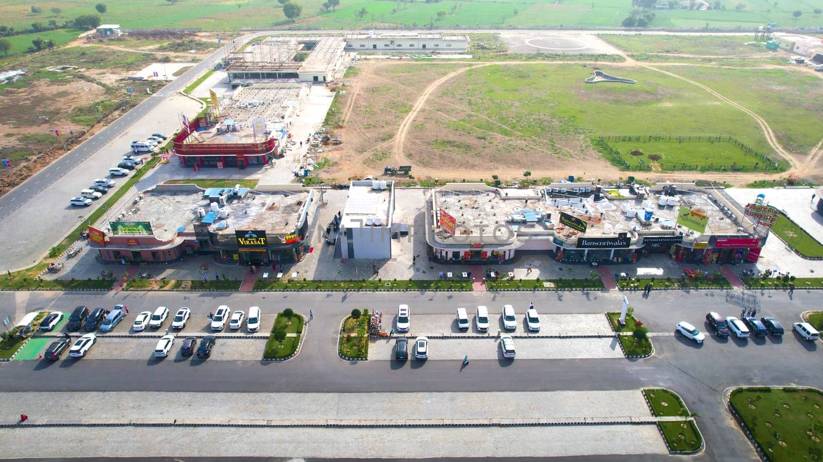 Delhi, India - 19th Feb 2025: Panning sideway aerial drone shot showing mix of branded food outlets in rest area midway of delhi Mumbai expressway with cars parked and huge green parks in distance showing rapid development in road network by NHAI