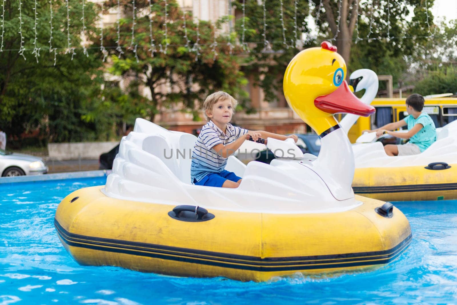 Child riding inflatable duck-shaped paddle boat on a shallow pool at an outdoor amusement park attraction