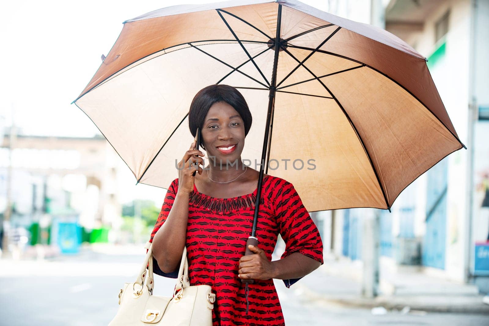 mature woman in traditional clothes standing talking on mobile phone smiling with umbrella over her head.