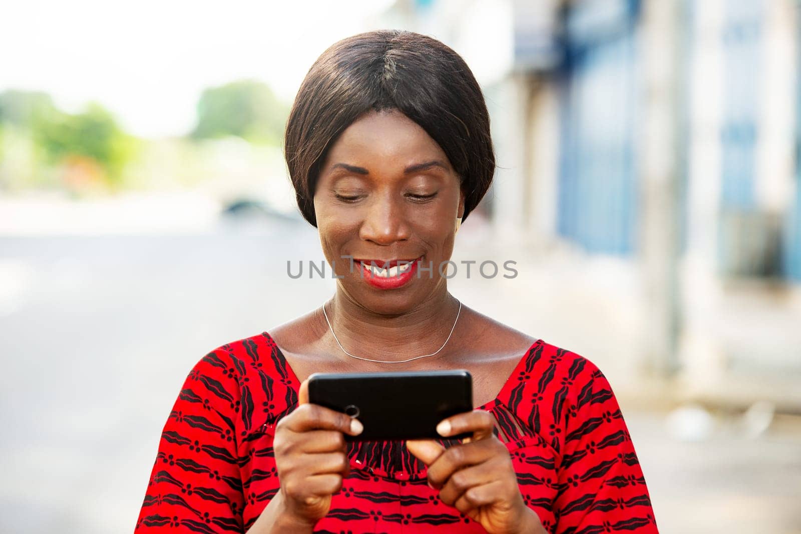 mature woman in traditional clothes standing outdoors looking at mobile phone while smiling.