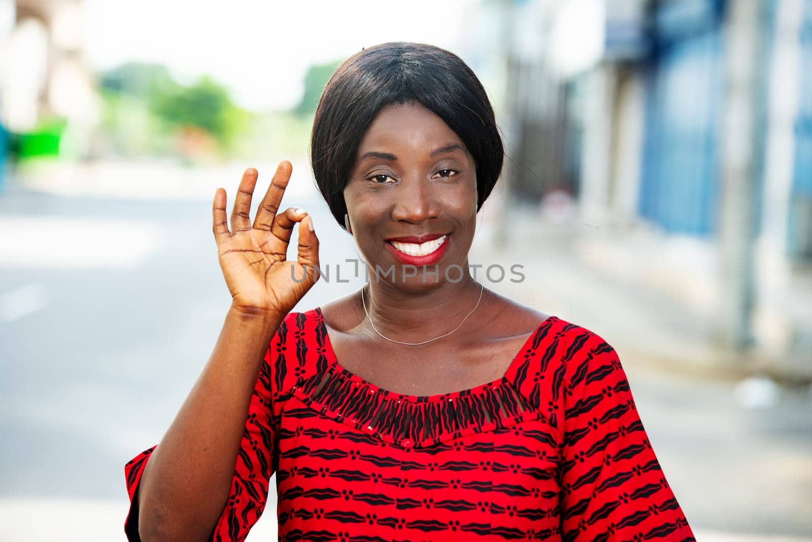 mature woman in traditional outfit standing outdoors looking at camera smiling and making hand gesture.