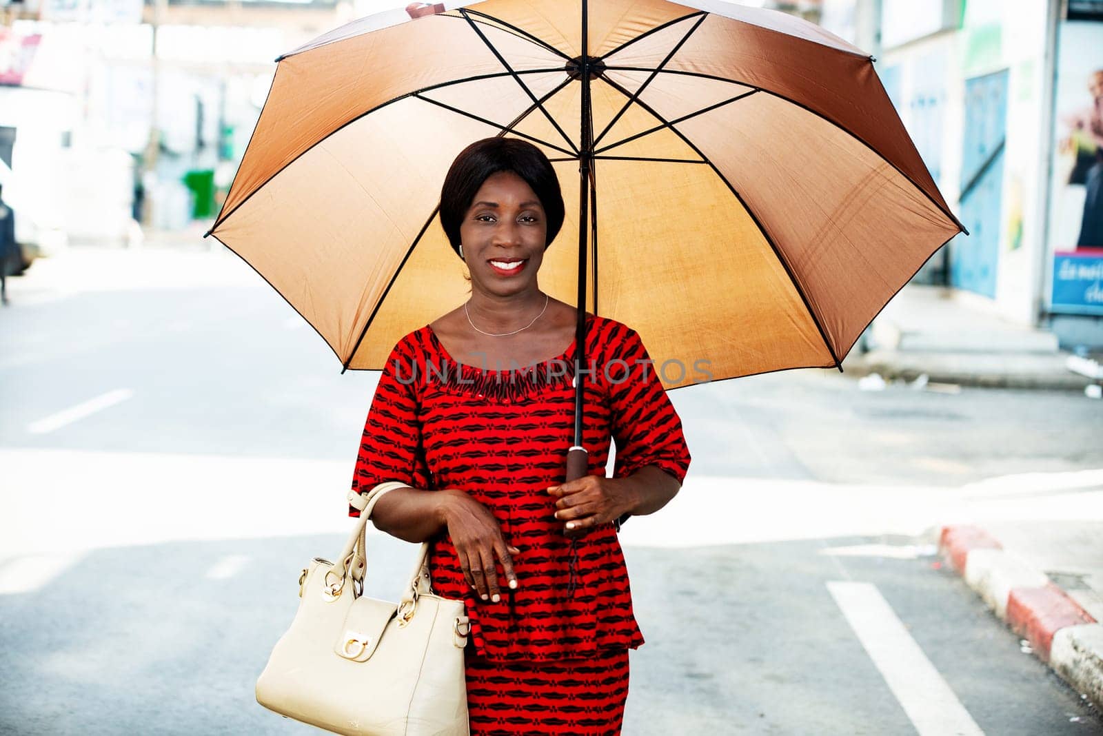 mature woman in traditional clothes standing outdoors looking at camera smiling with umbrella over her head