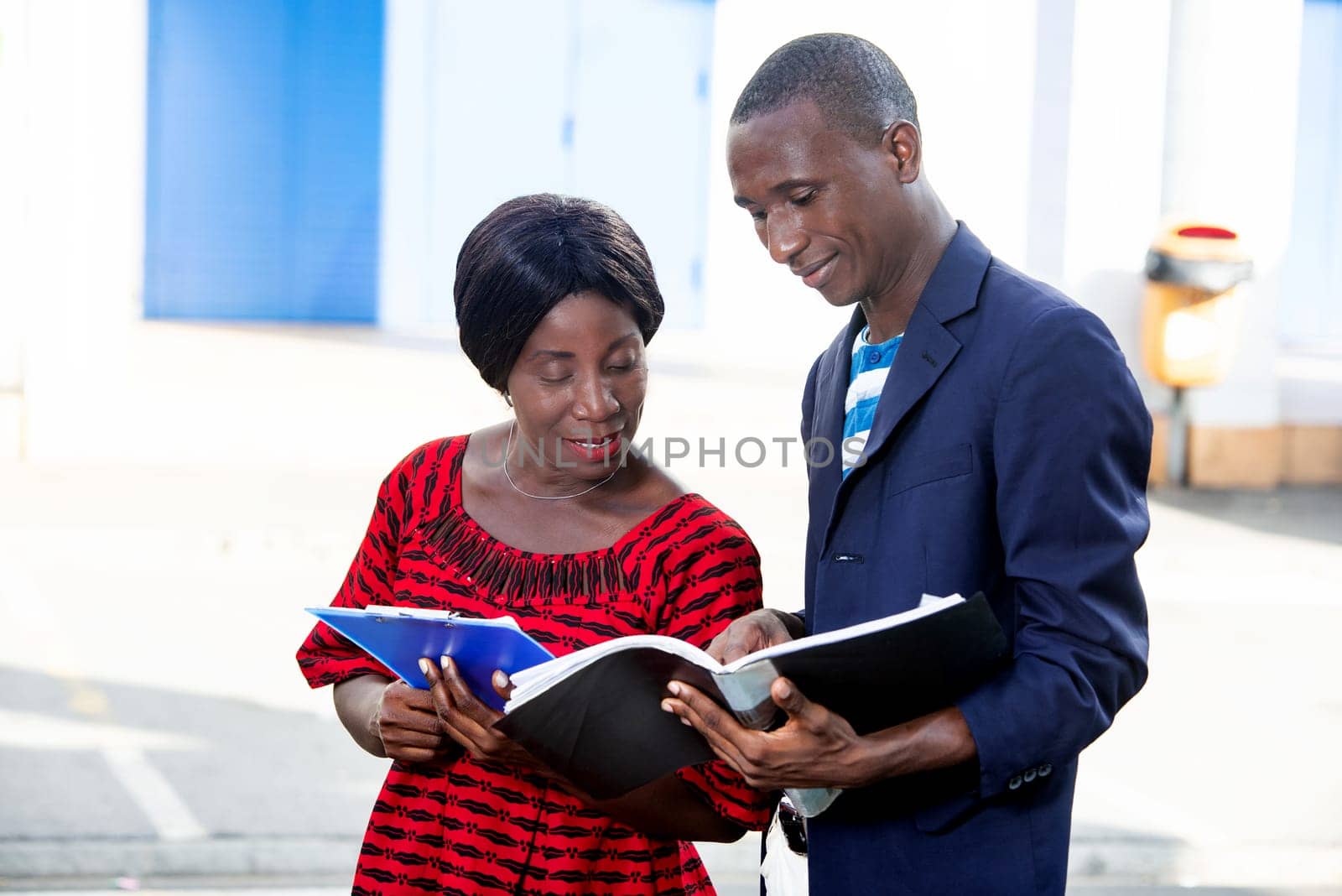 beautiful woman and handsome african adult businessman standing smiling, talking and displaying documents in the street