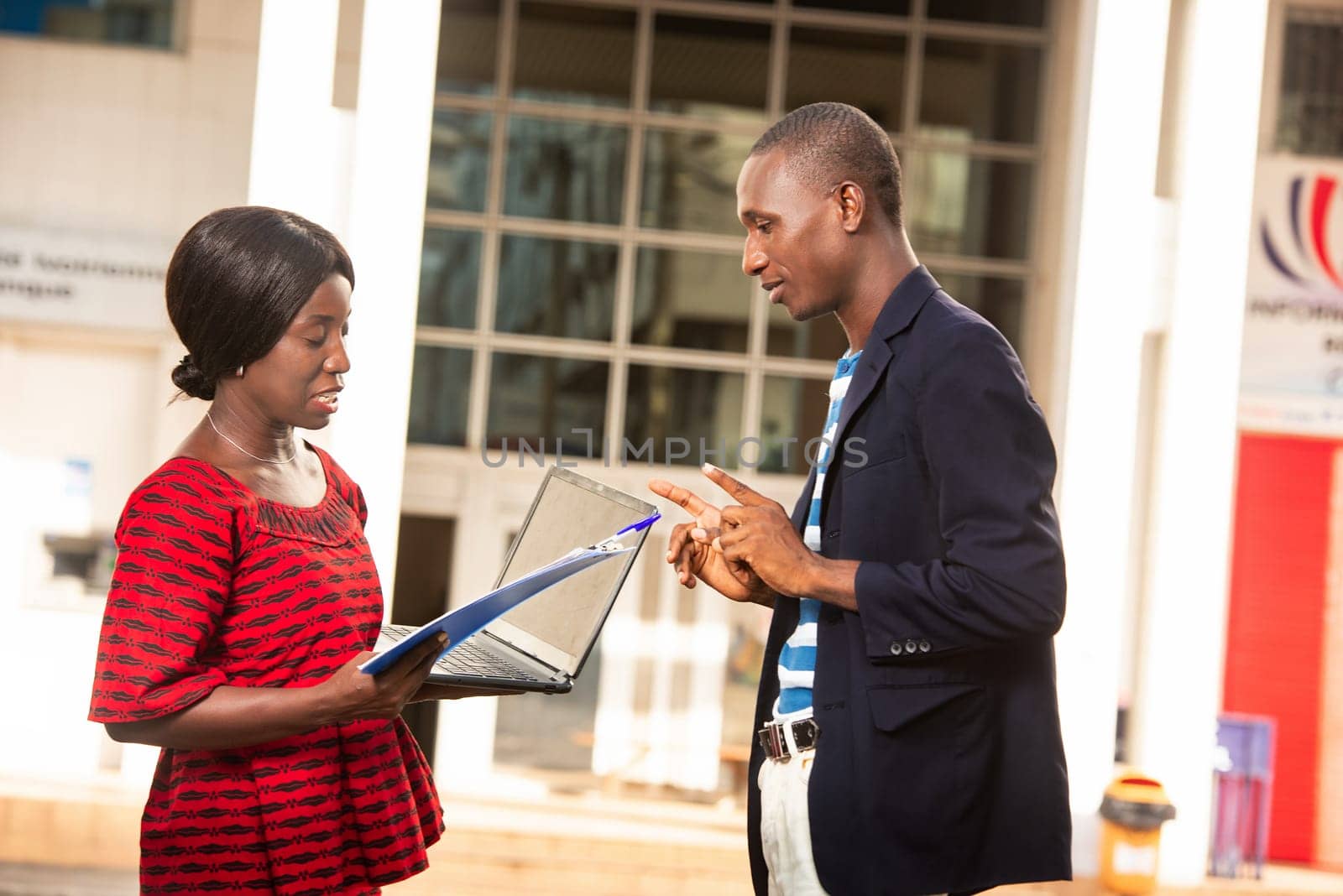 handsome african businessman giving project instructions to woman businesswoman holding computer and folders