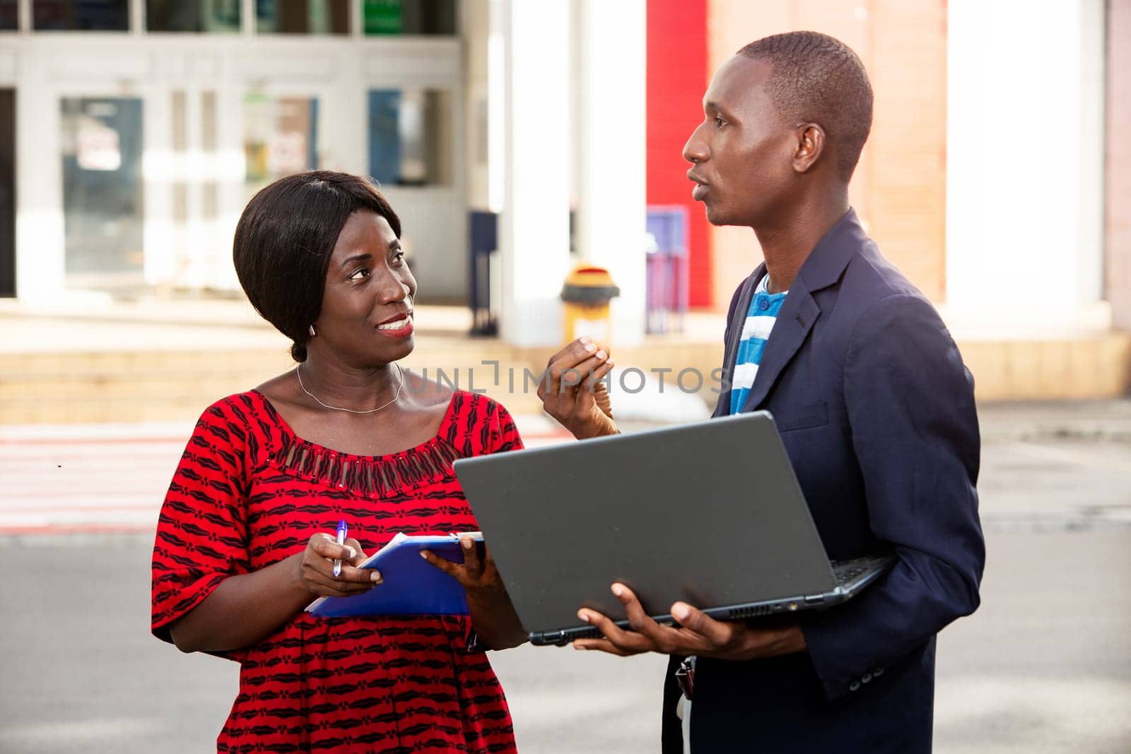 adult woman african and man working together on a project using a laptop on the street and a folder smiling on the street