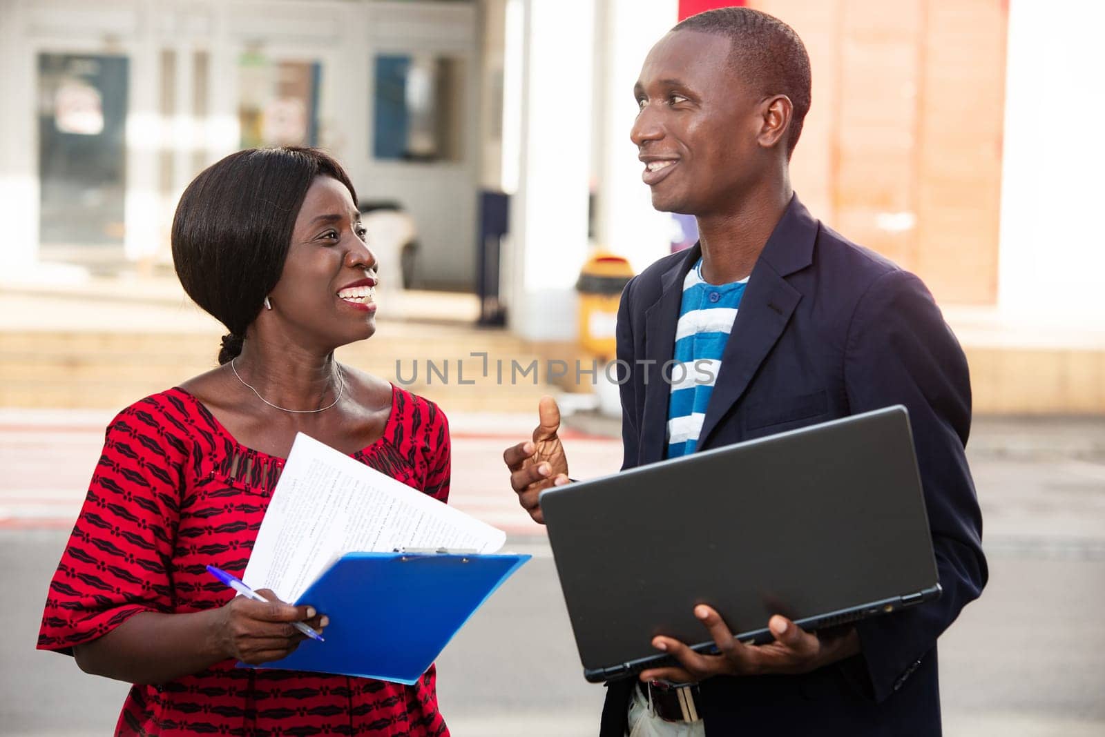 adult woman and a man working together on a project using a laptop in the street and a folders while smiling in the street