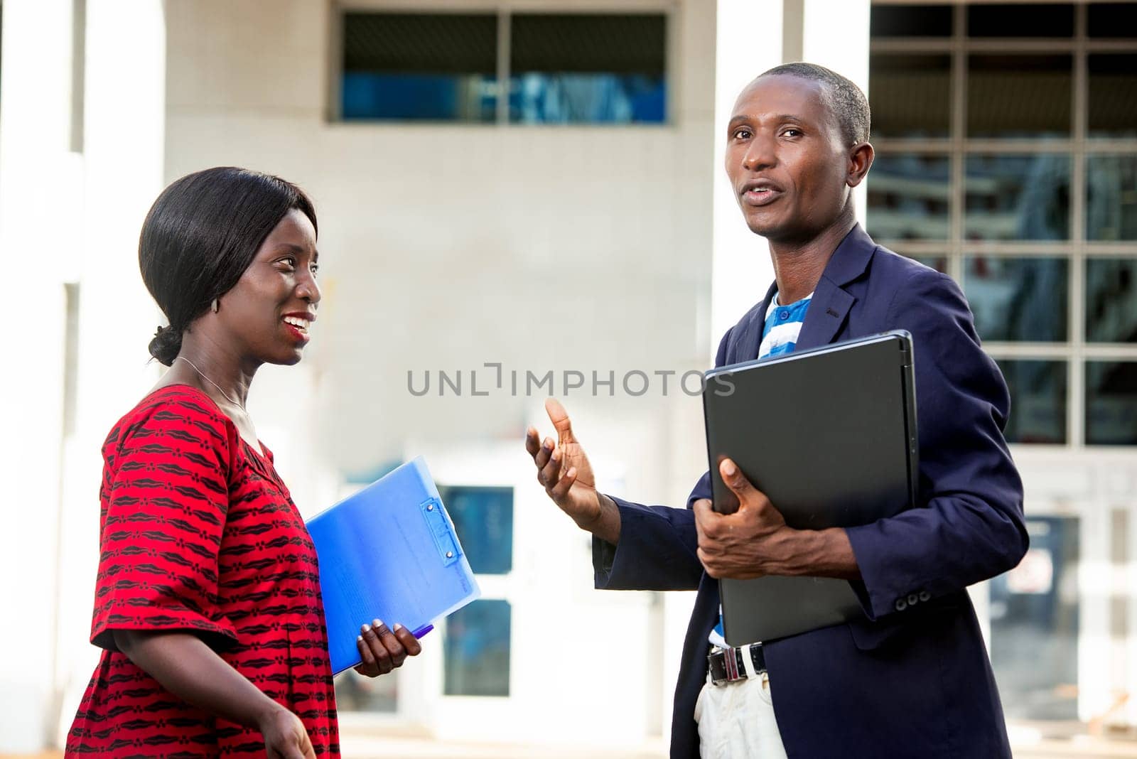beautiful African businesswoman discussing is discussing holding in hand a blue folder with a businessman holding a computer in the street