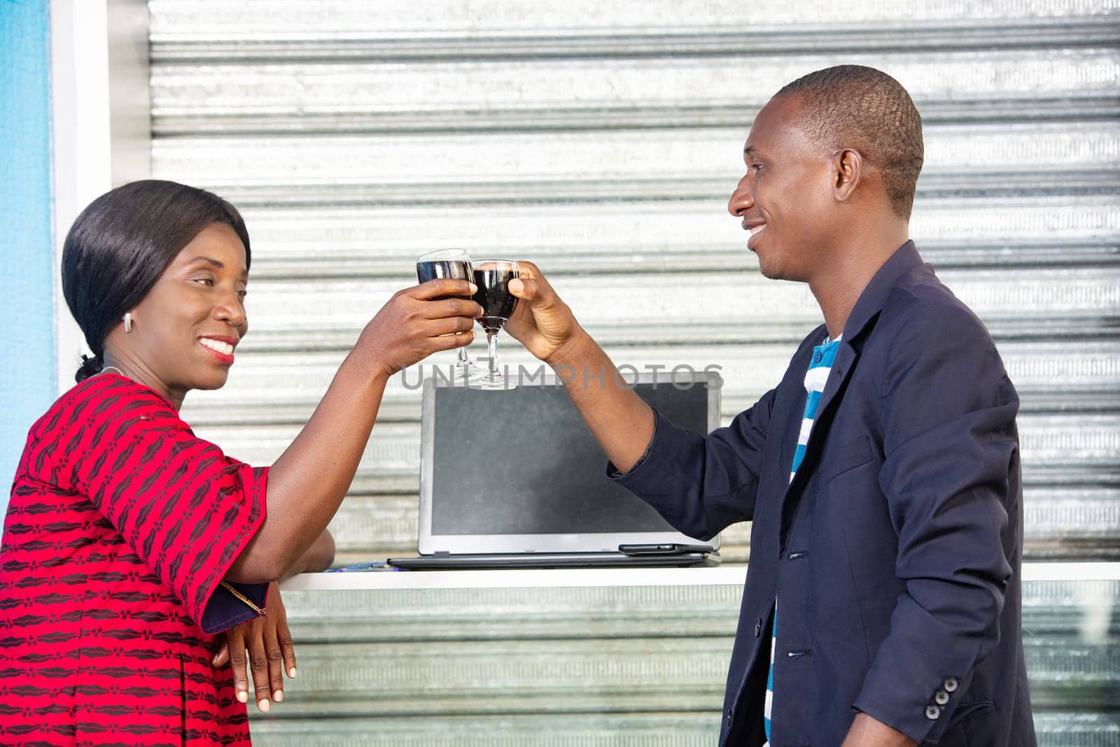 handsome adult african man and adult business woman are celebrating a win by drinking a glass of red wine outside, while being smiling
