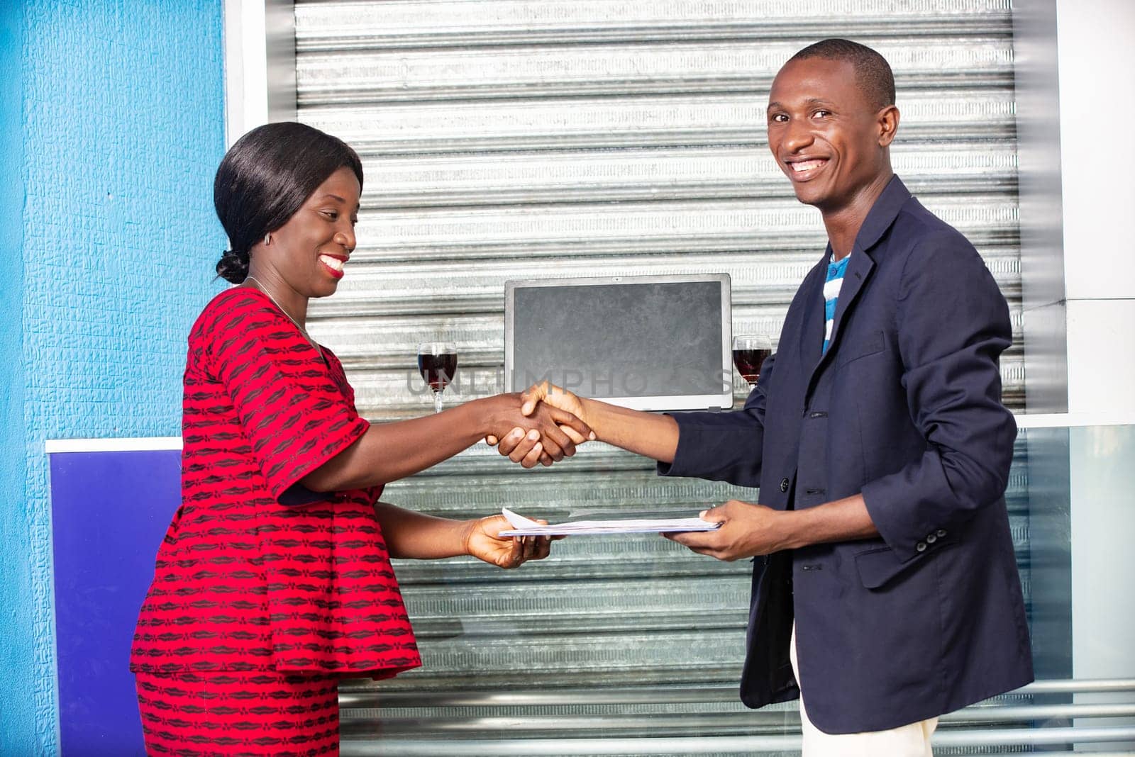 Professional business woman and man in formal suit shaking hands outside to make an agreement exchanging documents while smiling