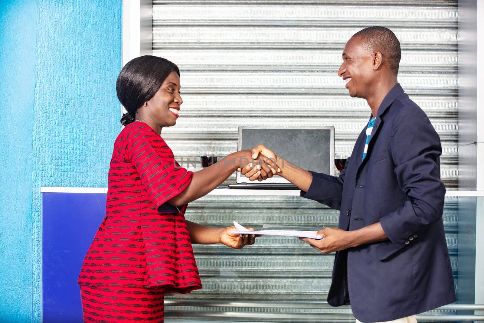 Professional business woman and man in formal suit shaking hands outside to make an agreement exchanging documents while smiling