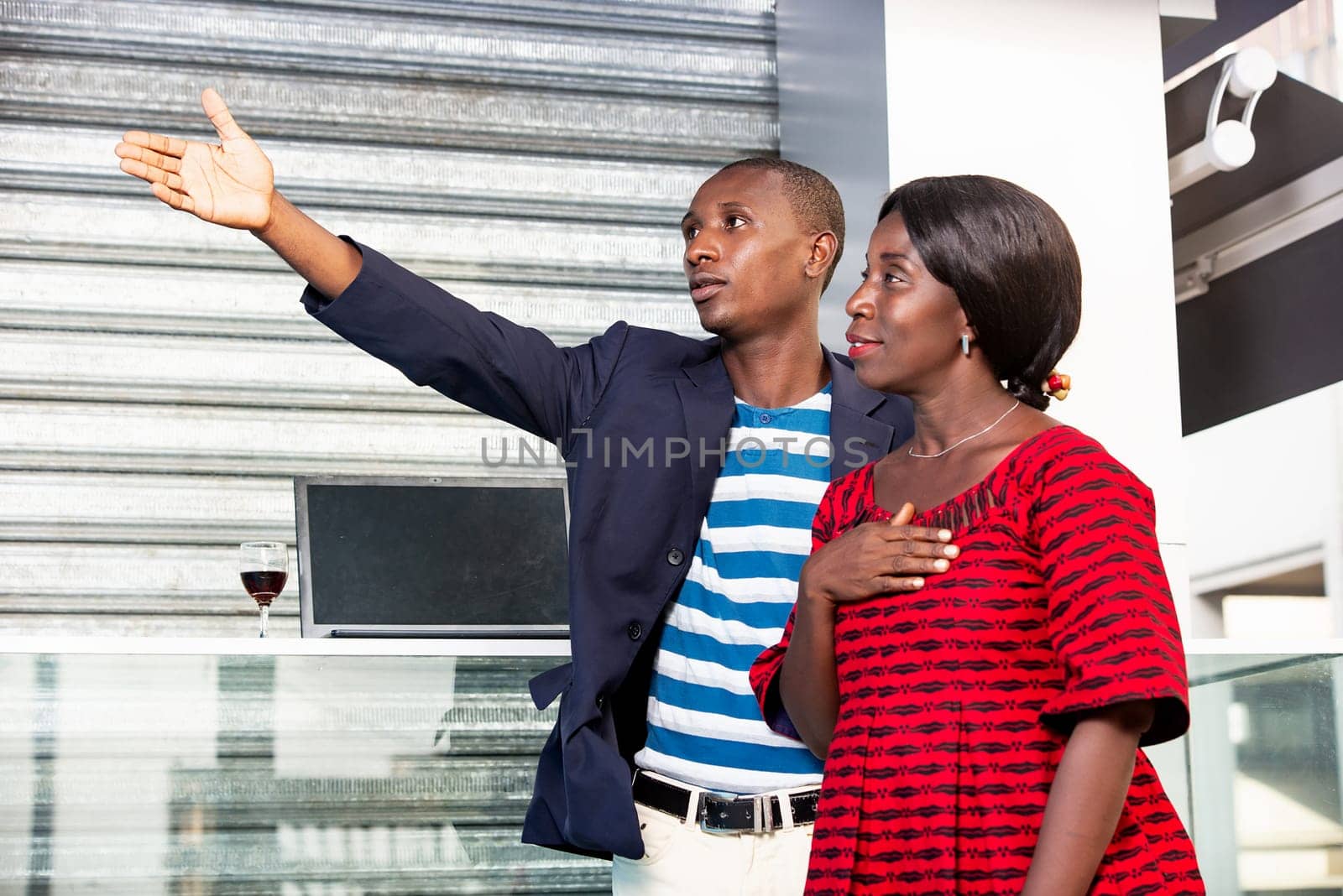 African man wearing a jacket pointing finger pointing at the direction of the businesswoman holding hands on the heart while smiling