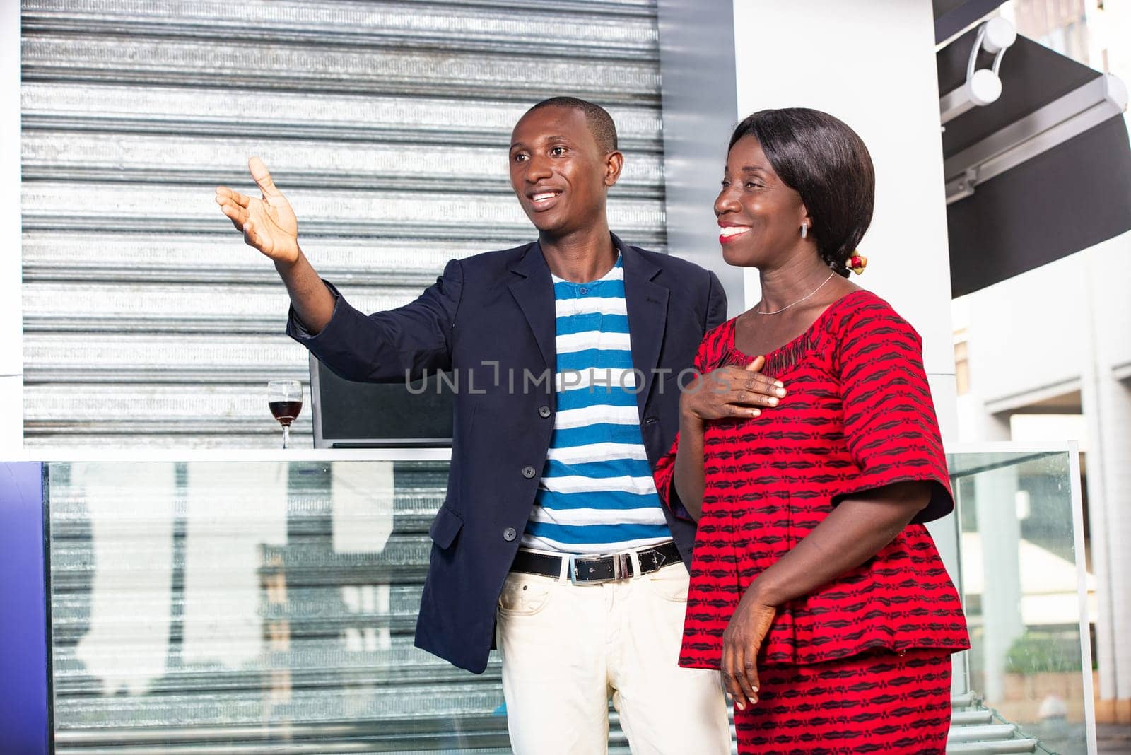 African man wearing a jacket pointing the finger in the direction of the businesswoman holding hands on the heart while smiling