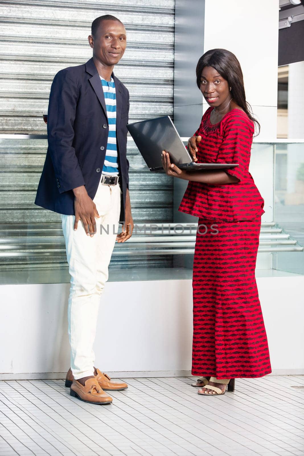 Photo of handsome businessman and beautiful woman as business partners outdoors holding a computer while smiling