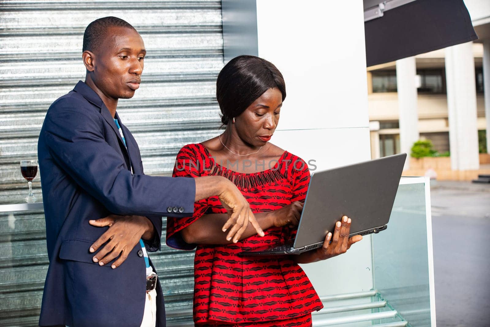 handsome African adult man and woman as business partners working with a laptop in the street