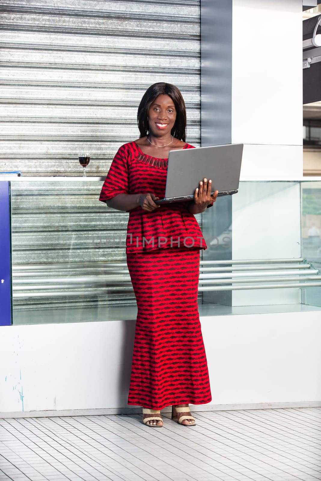 beautiful adult businesswoman dressed in red loincloth suit is standing using a laptop while being smiling