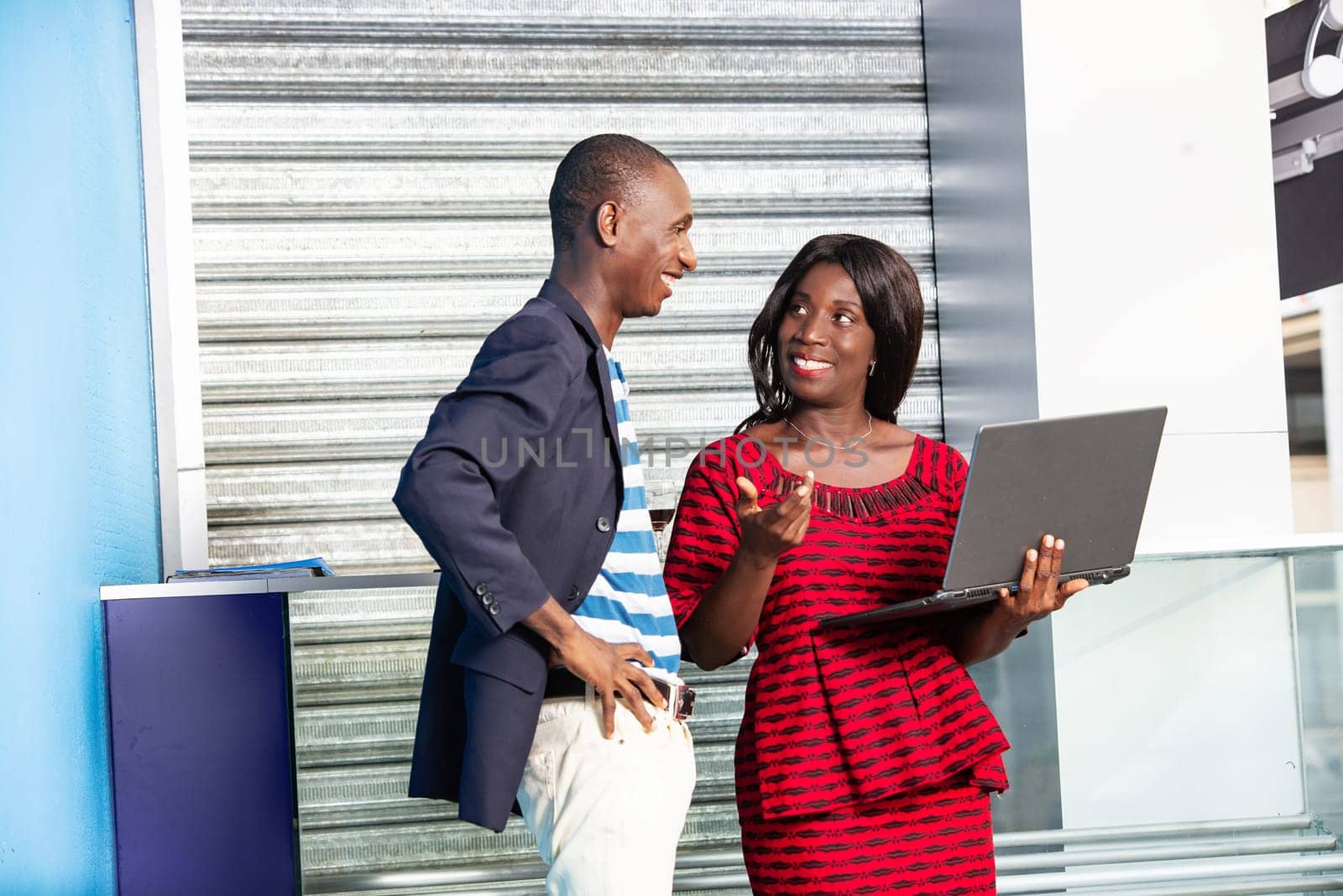 Handsome businessman and african businesswoman working using a laptop together smiling in the street