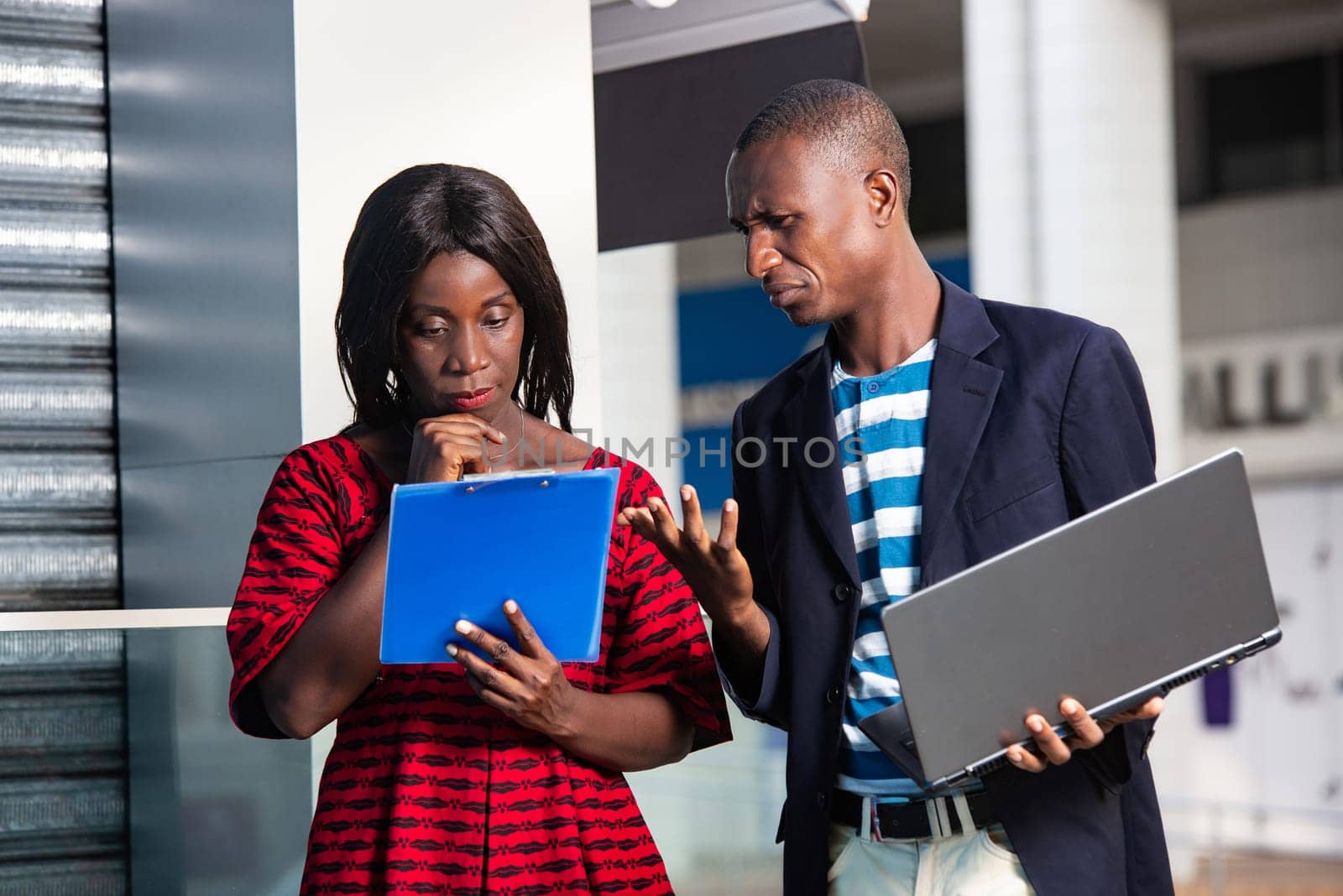 businessman holding a computer chatting with businesswoman holding the folder with documents in hand outside