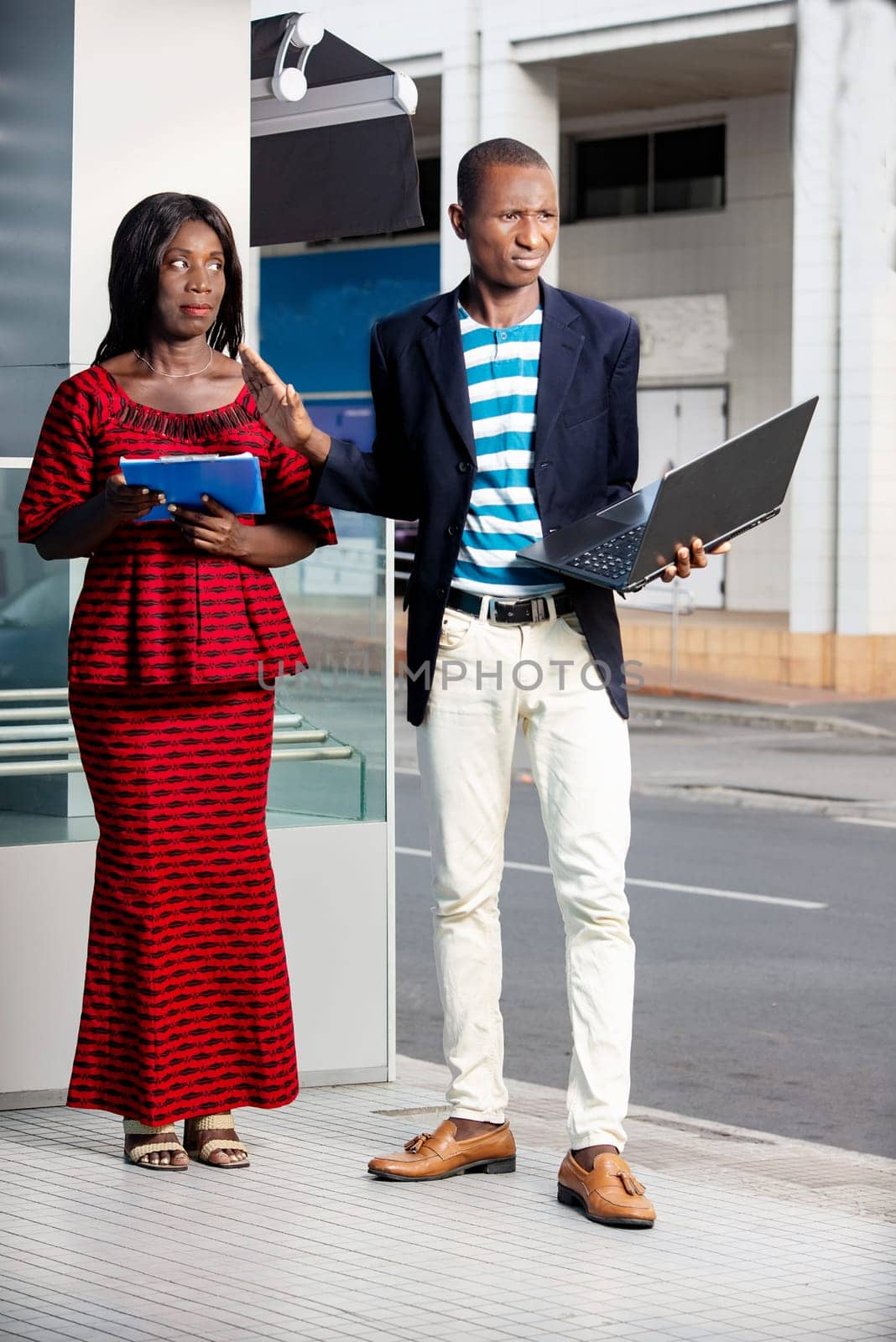 businessman holding a computer chatting with businesswoman holding the folder with documents in hand outside