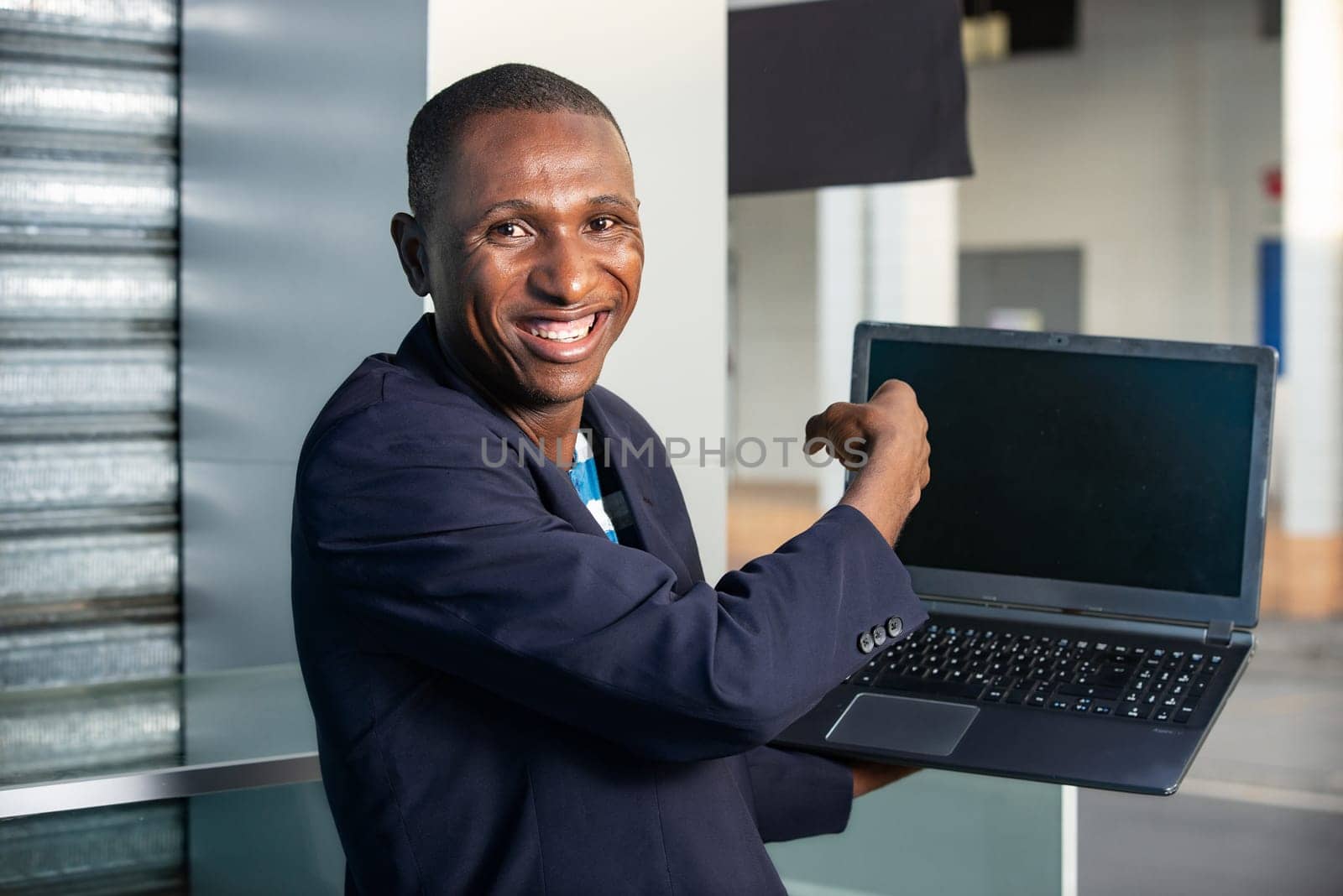 handsome adult businessman making a gesture pointing to show a laptop while being happy on the street