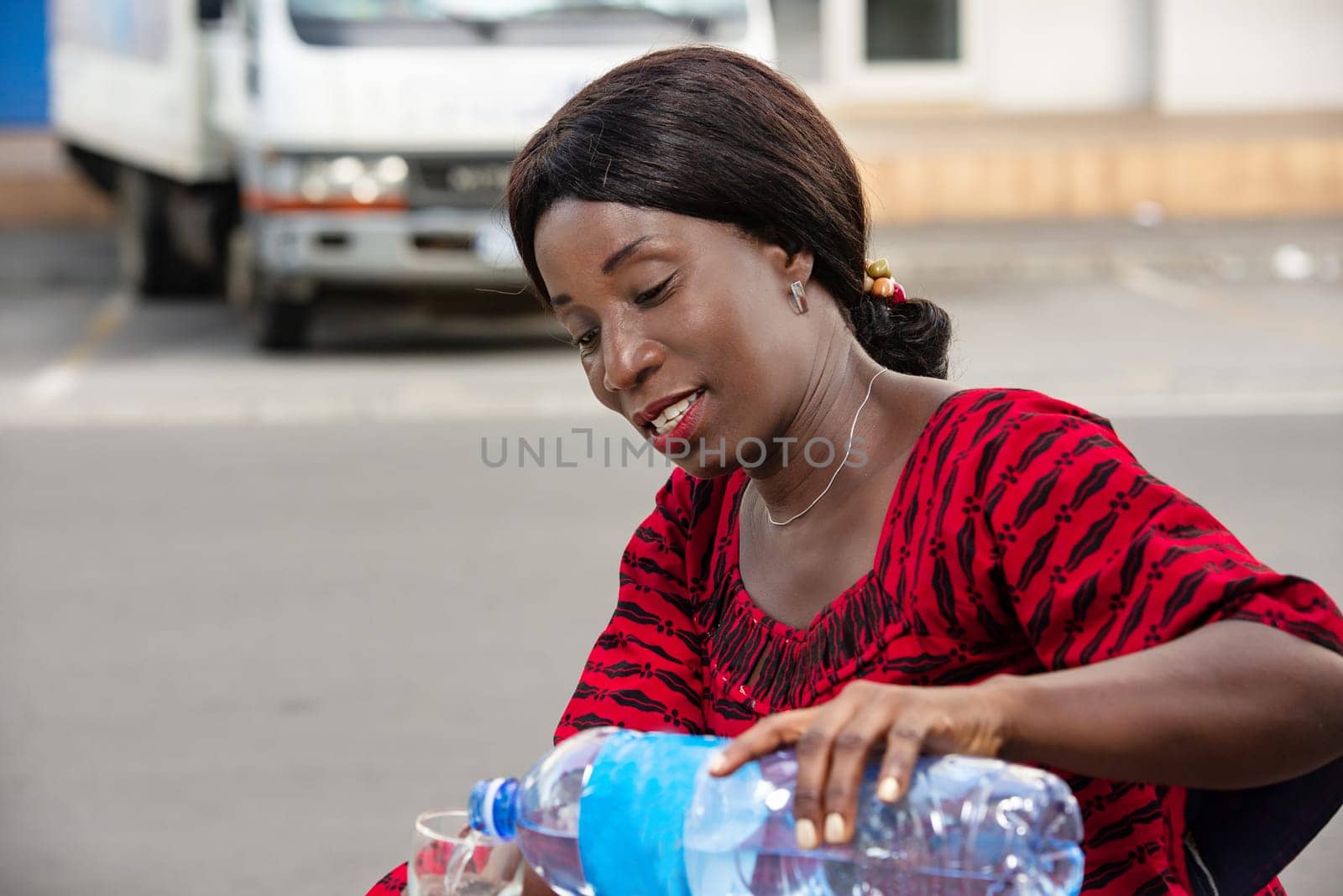 mature woman sitting outdoors in traditional outfit serving water in a glass smiling.