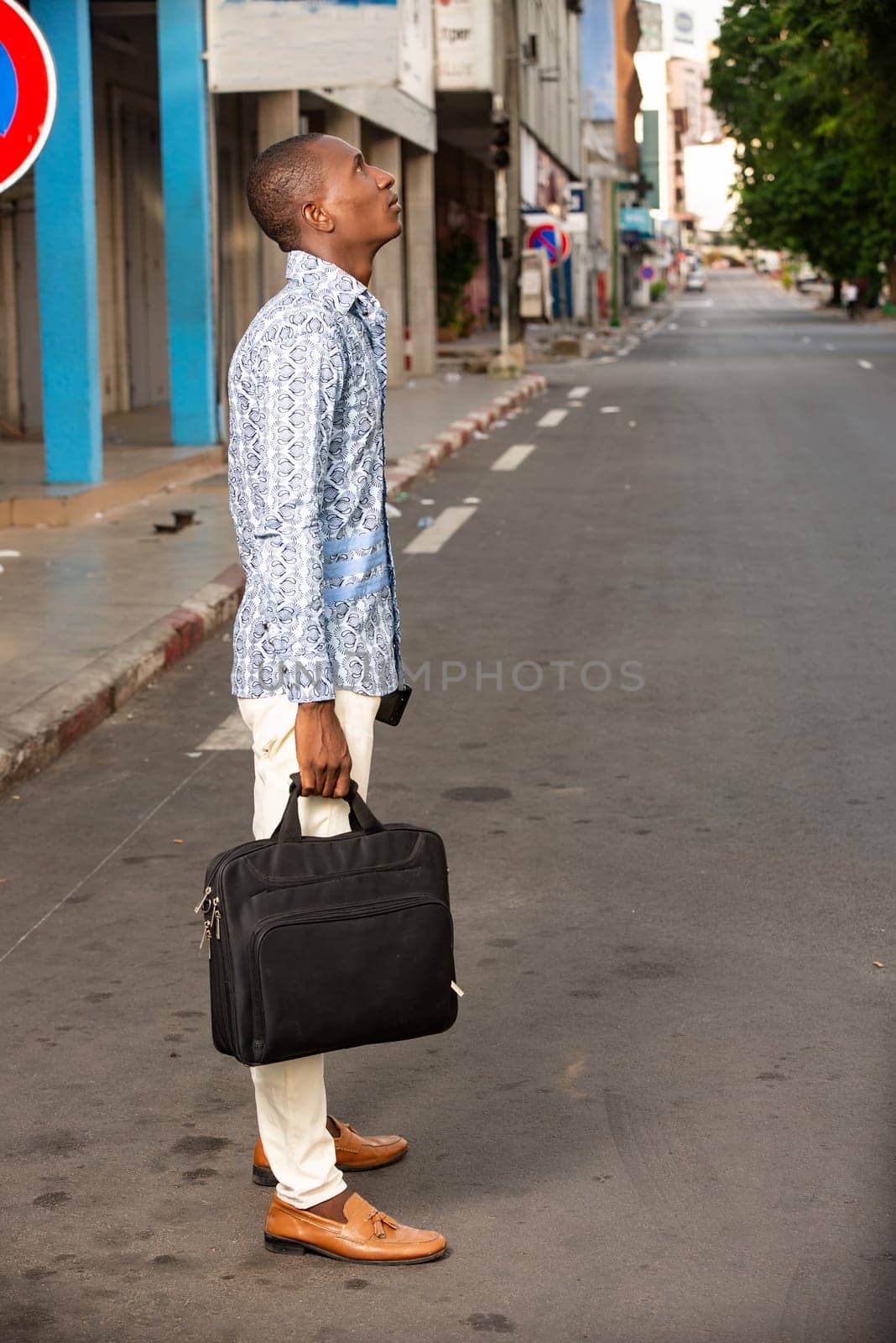 young businessman standing outdoors thinking about holding a bag.