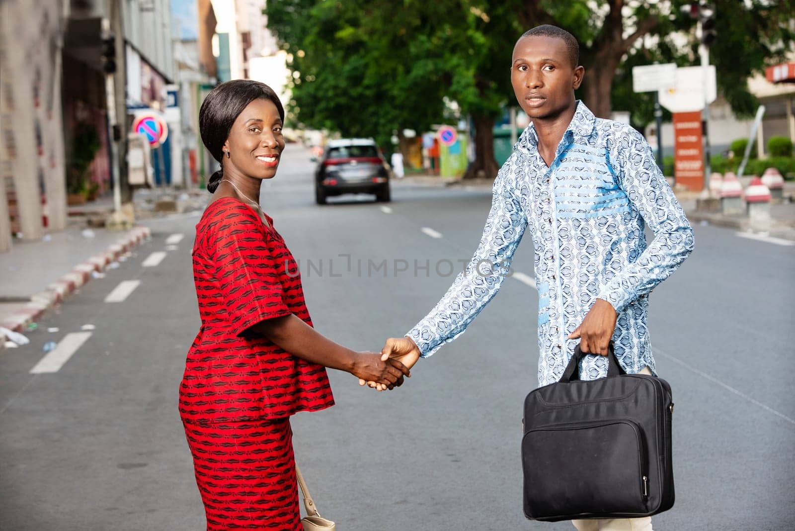 young businessman standing outdoors in traditional dress shaking hands with his partner smiling.