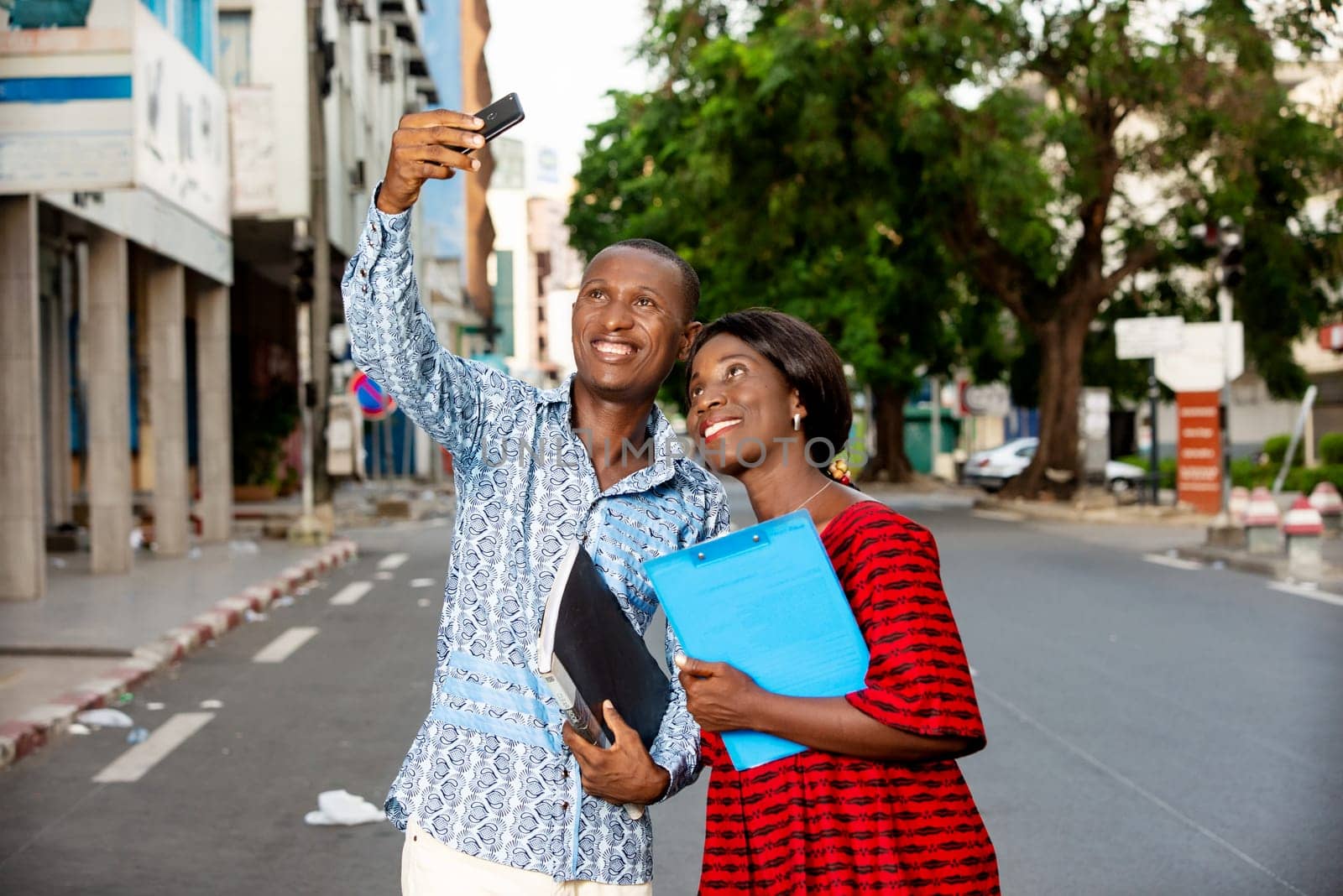 african business people smile while looking at a funny photo or watching a video on the mobile phone with documents in hands outdoors