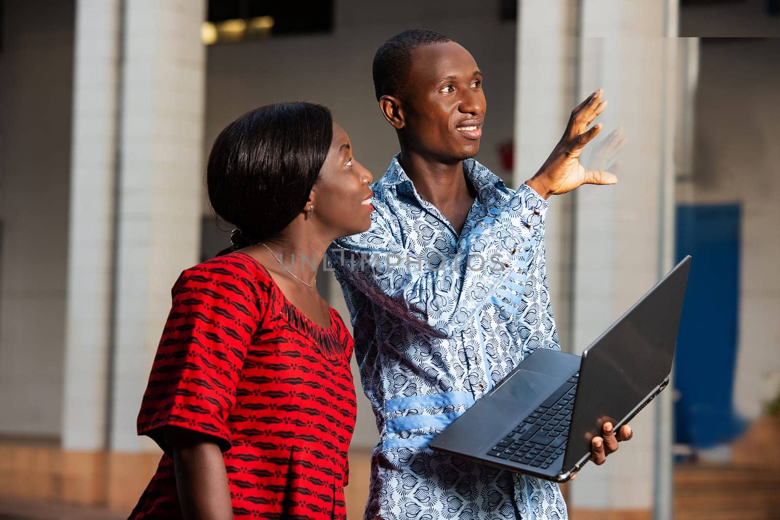 Young businessman discussing work using a laptop with a woman outdoors in town.