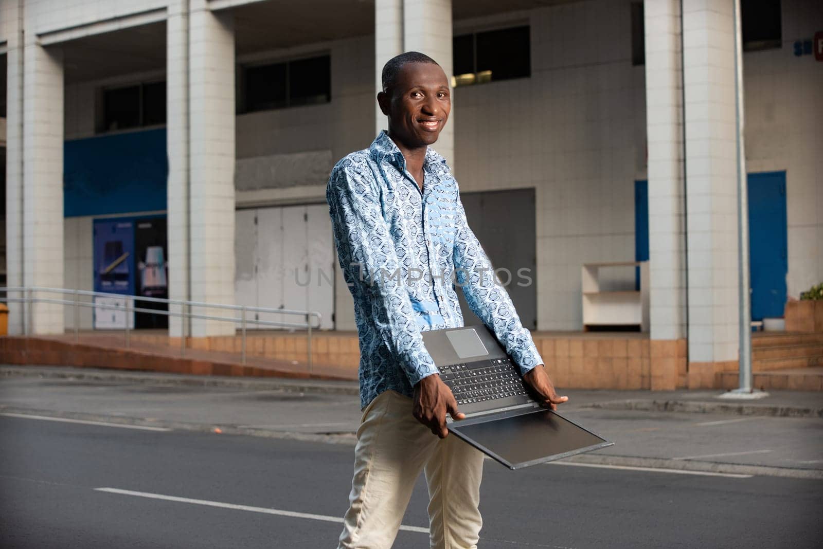 Happy african adult man standing smiling using a laptop in hand on the street