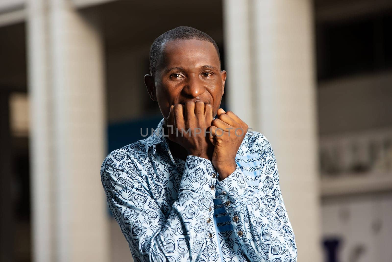 African stressed and nervous adult man with hands on mouth while biting his nails in the street