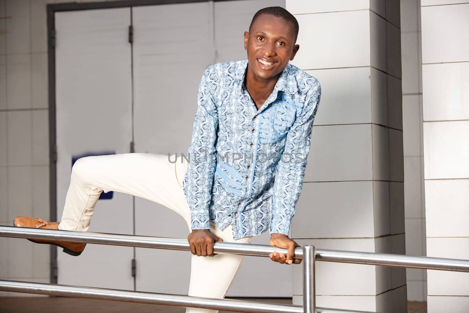 young man in traditional clothes jumping iron bar and looking at camera smiling.