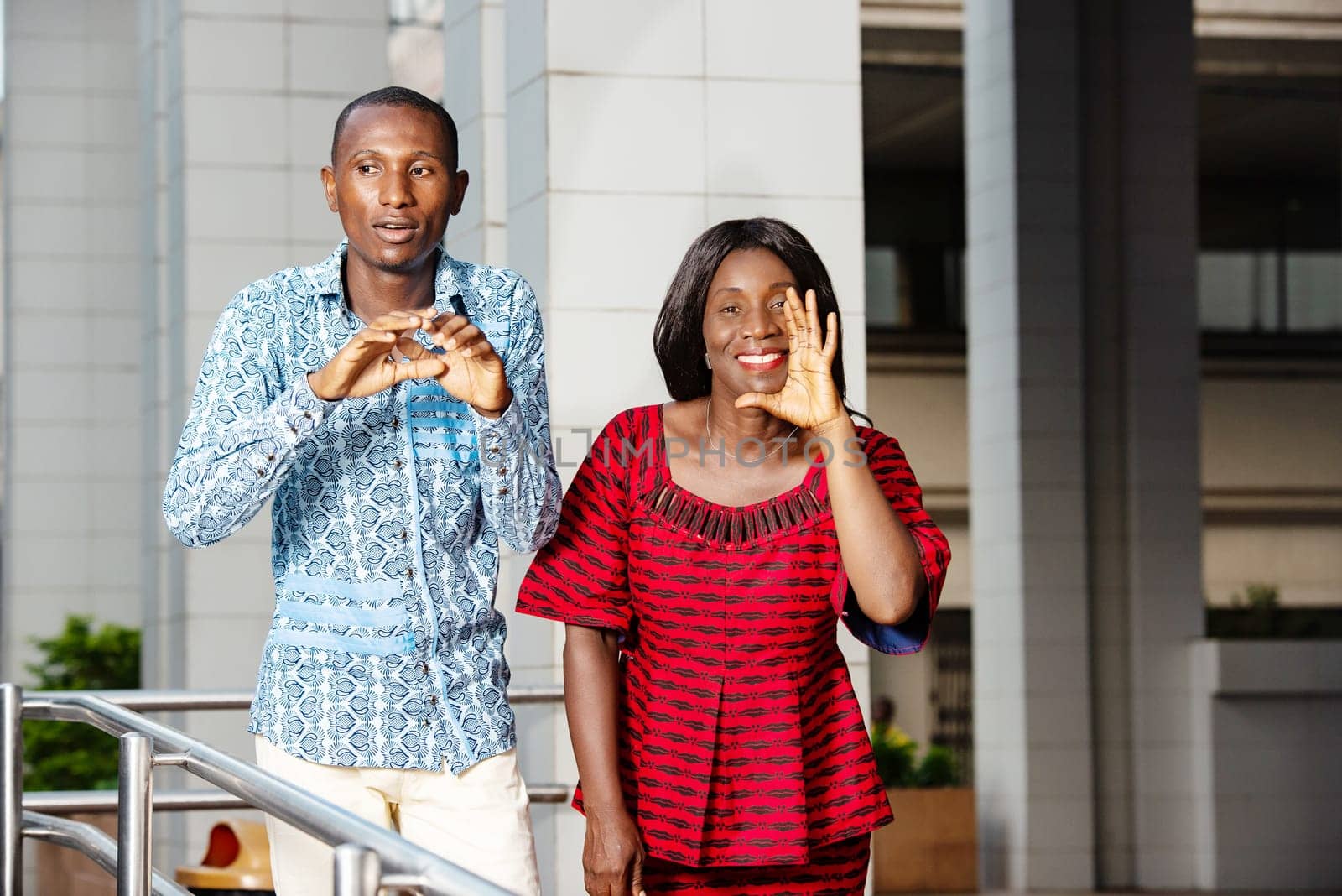two business people standing in traditional clothes beckoning to someone smiling.