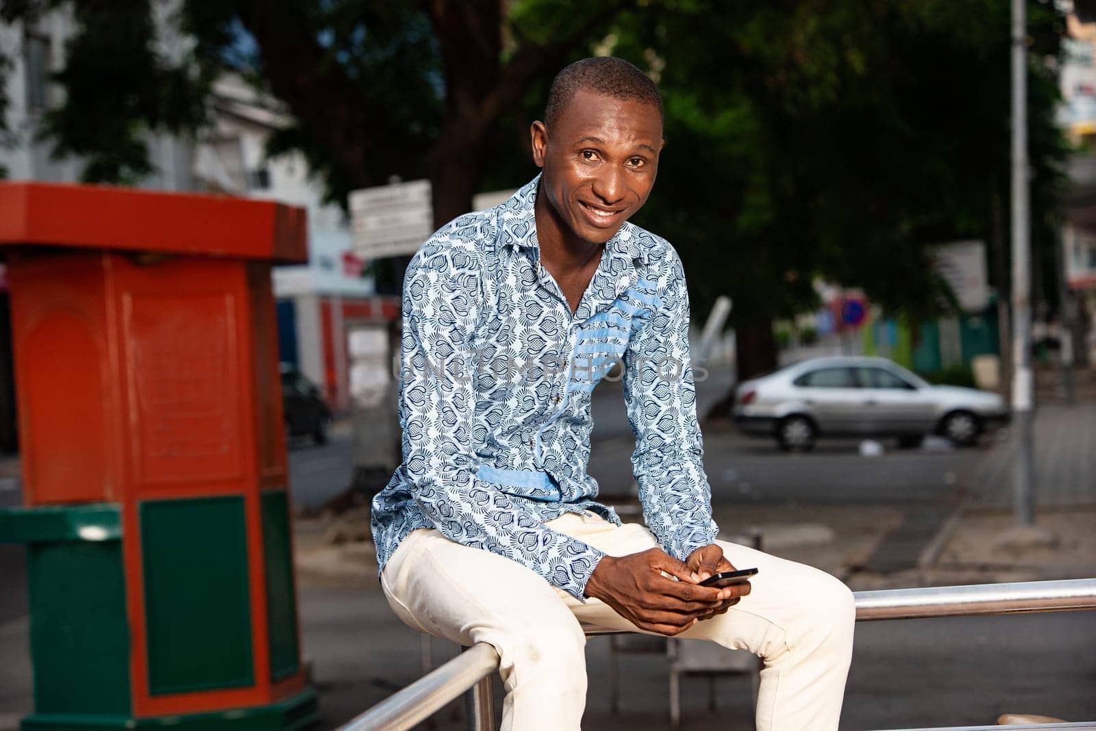 handsome adult african man sitting in the street using his mobile phone