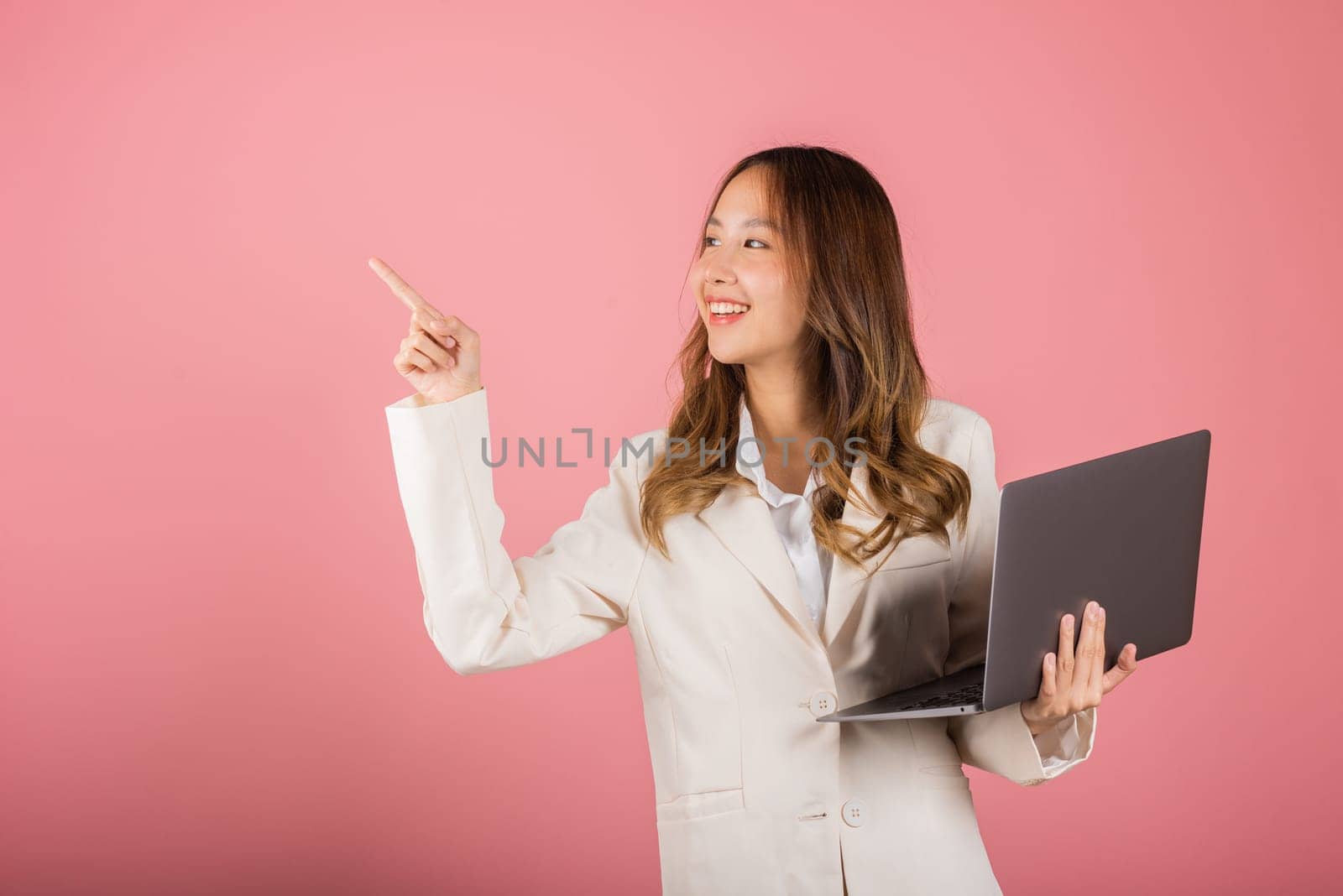 Portrait business woman holding laptop point finger empty space studio shot isolated on pink background, Young smiling happy fun attractive cheerful skilled female hold computer with copy space
