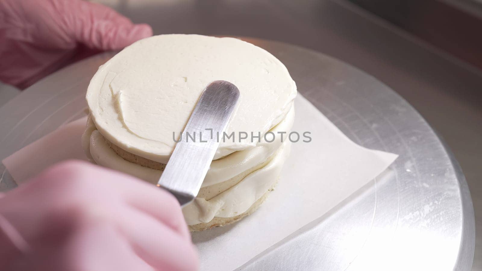 Female professional hands levels cream on baked sponge cake using metallic pastry scraper. Dessert decor. Pastry decoration. High quality