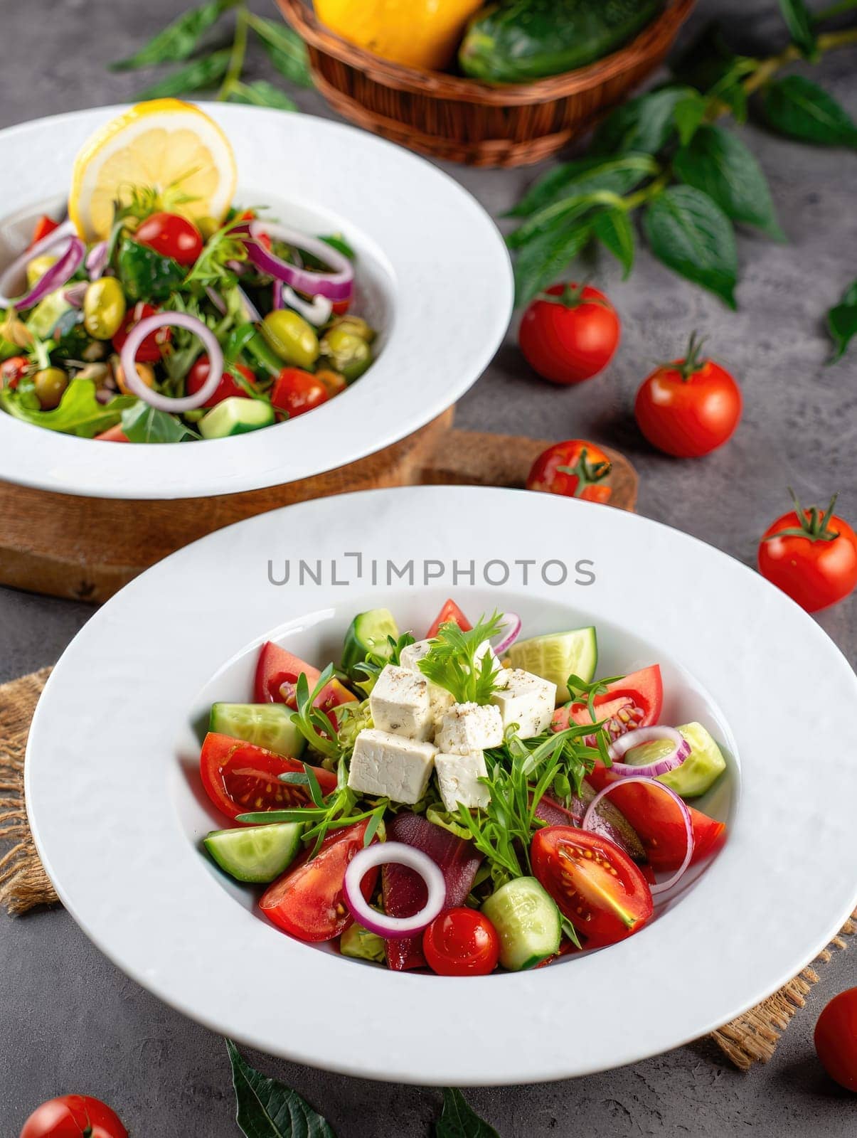 Two colorful salads featuring fresh tomatoes, cucumbers, red onions, and feta cheese served in white bowls. A lemon slice decorates one salad, enhancing the presentation.