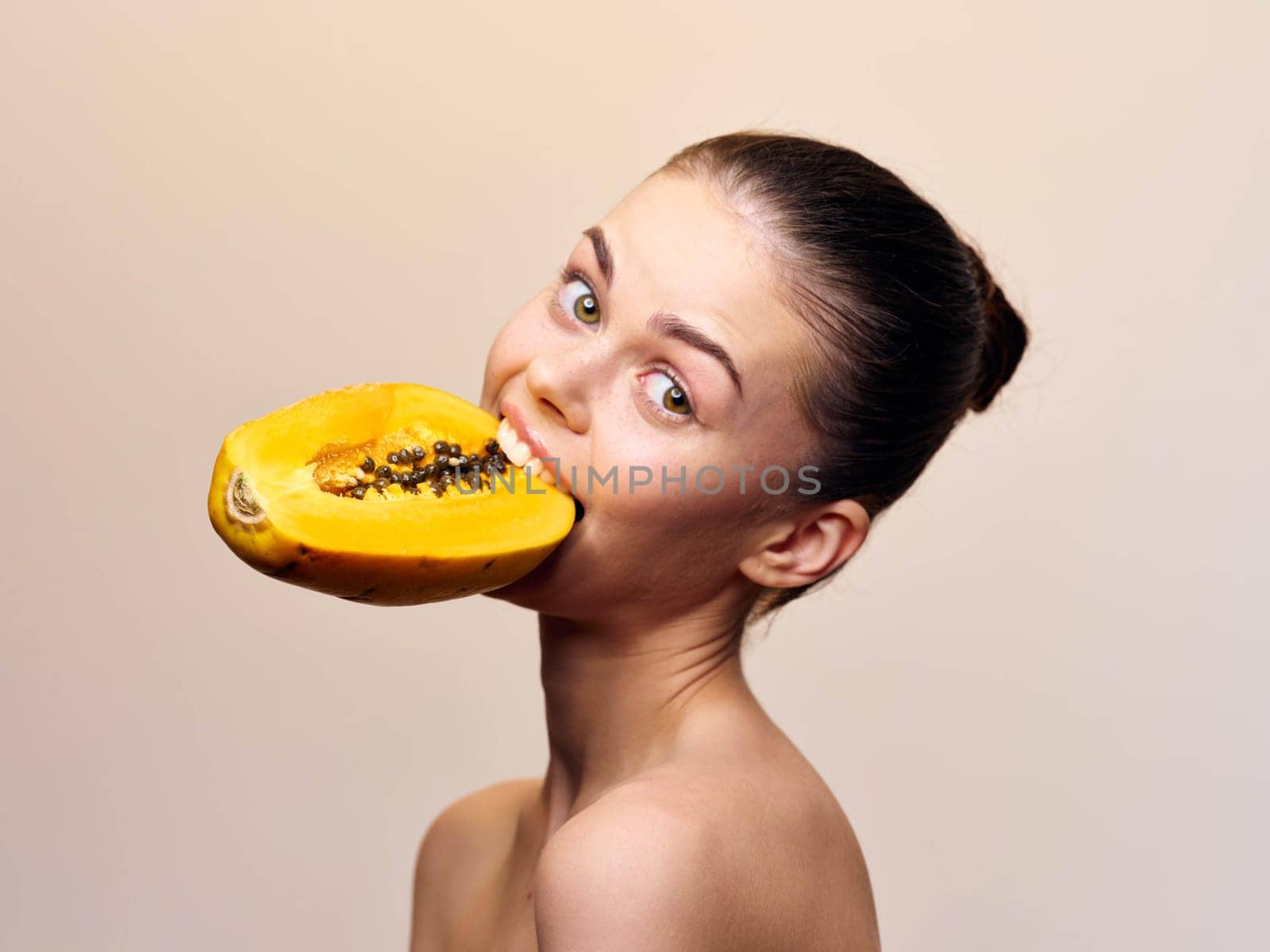 Gorgeous young woman enjoying fresh papaya fruit against beige background in studio shot