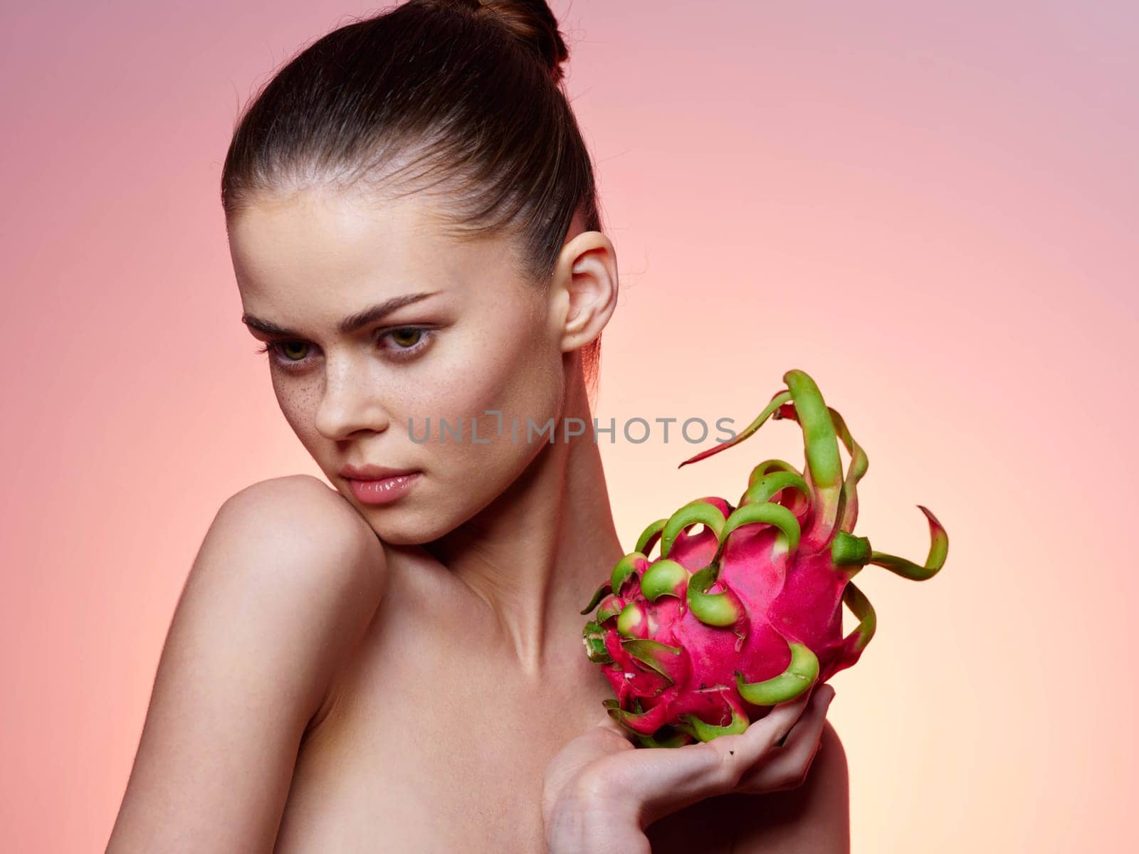 Beautiful young woman holding a fresh dragon fruit against a vibrant pink background in a stylish and modern stock photo
