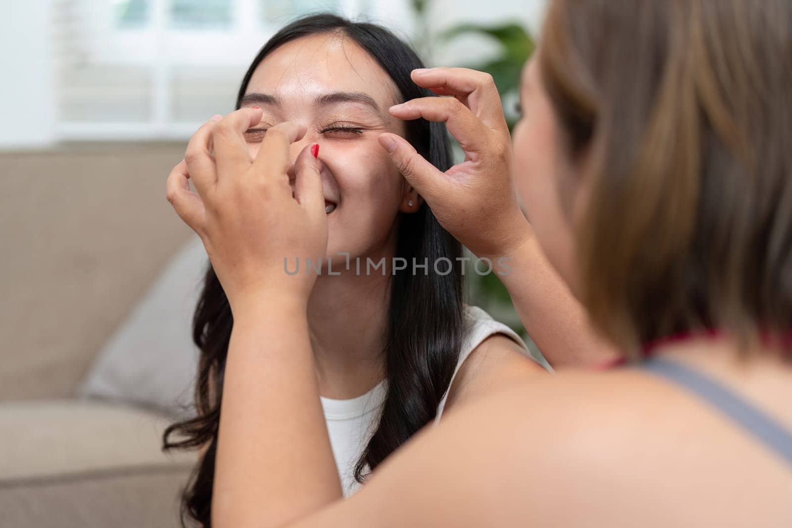 With the help of her friend, a woman smiles as she experiences a playful makeup moment, trying new looks and enjoying the process of self-expression.