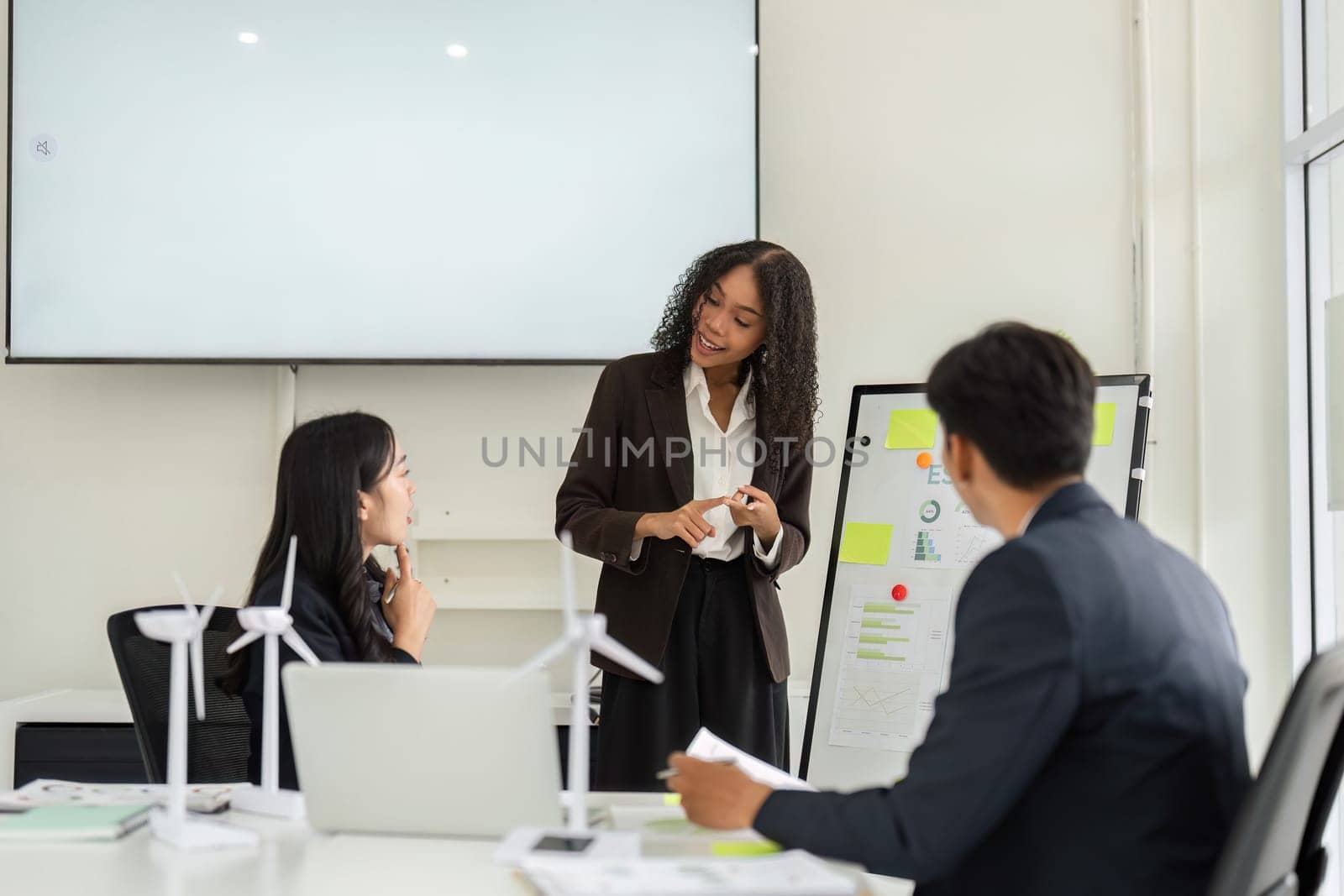During a collaborative meeting, a woman enthusiastically shares ESG performance metrics while her colleagues engage in the conversation, emphasizing teamwork and innovation.