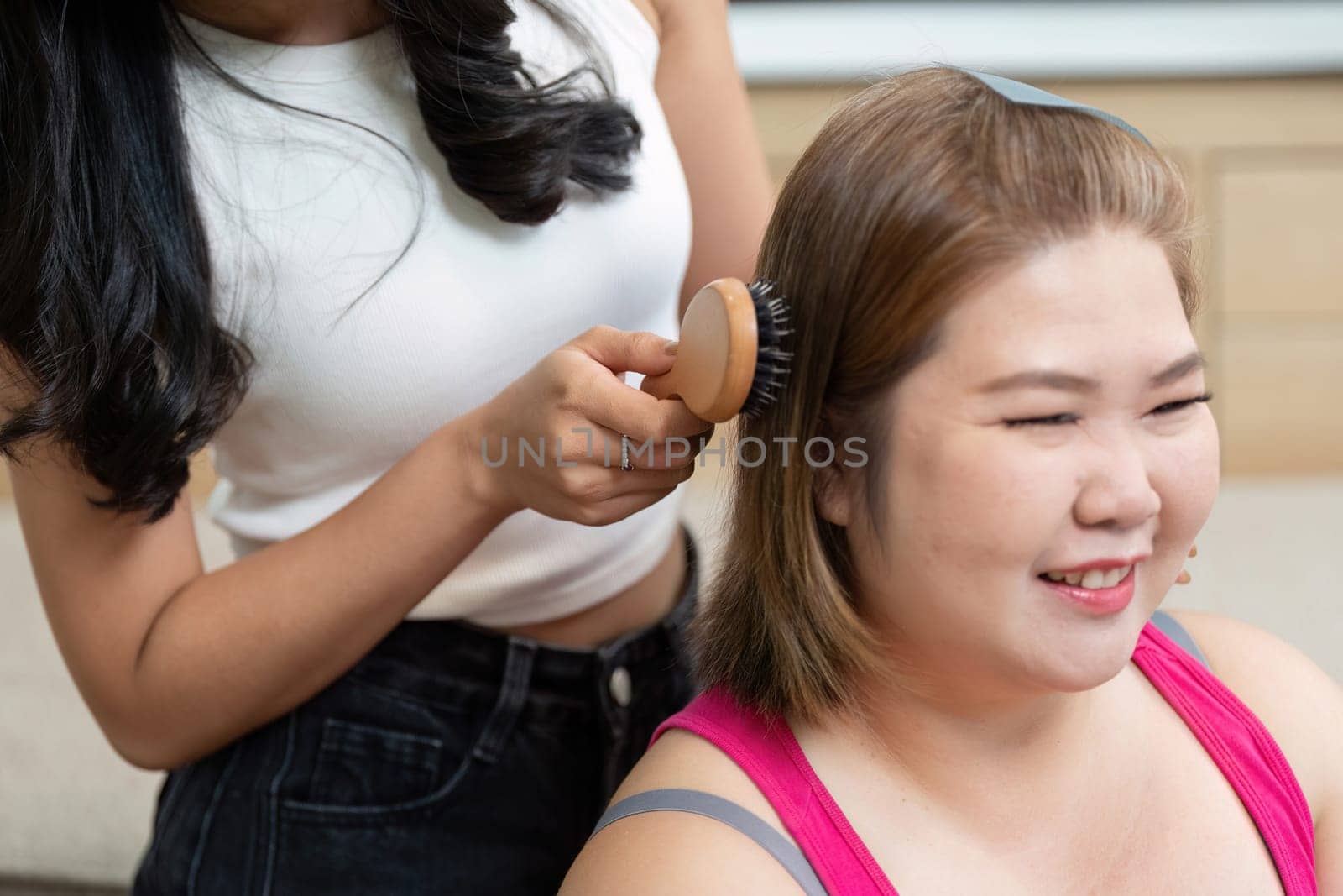 Two friends engage in a beauty session, highlighting the joy of friendship as one styles the other's hair, capturing a playful, relaxed atmosphere.