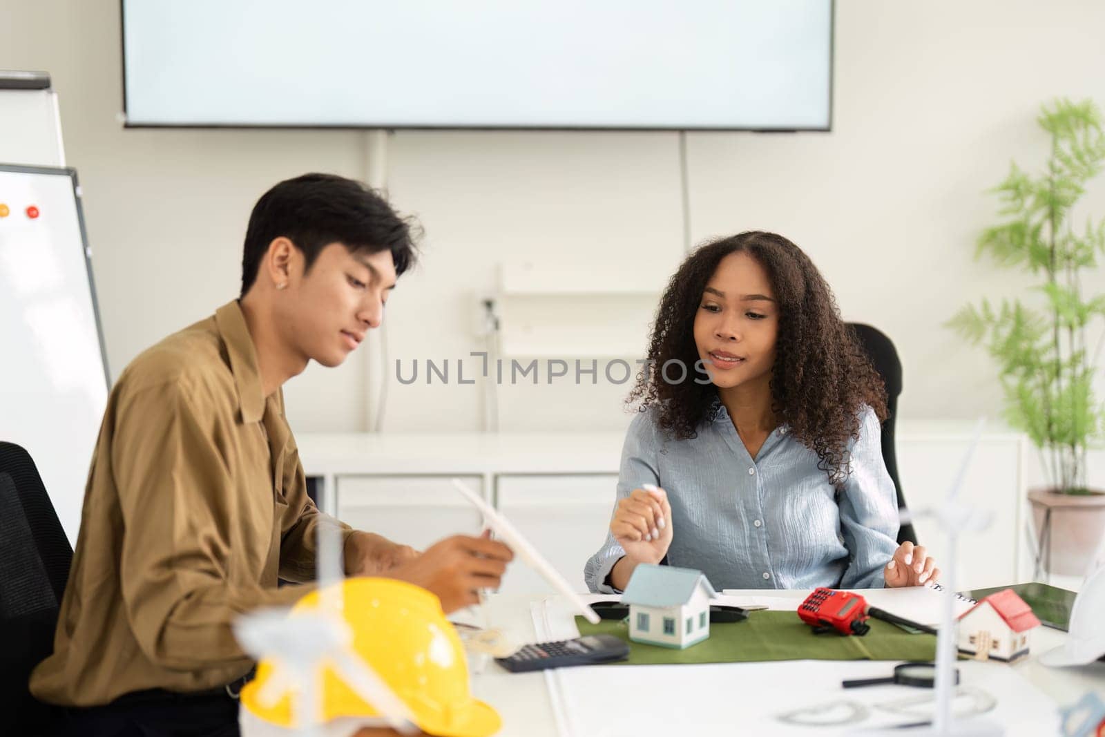 Two architects or engineers engaged in a discussion about sustainable architectural solutions, surrounded by models and tools in a contemporary office.