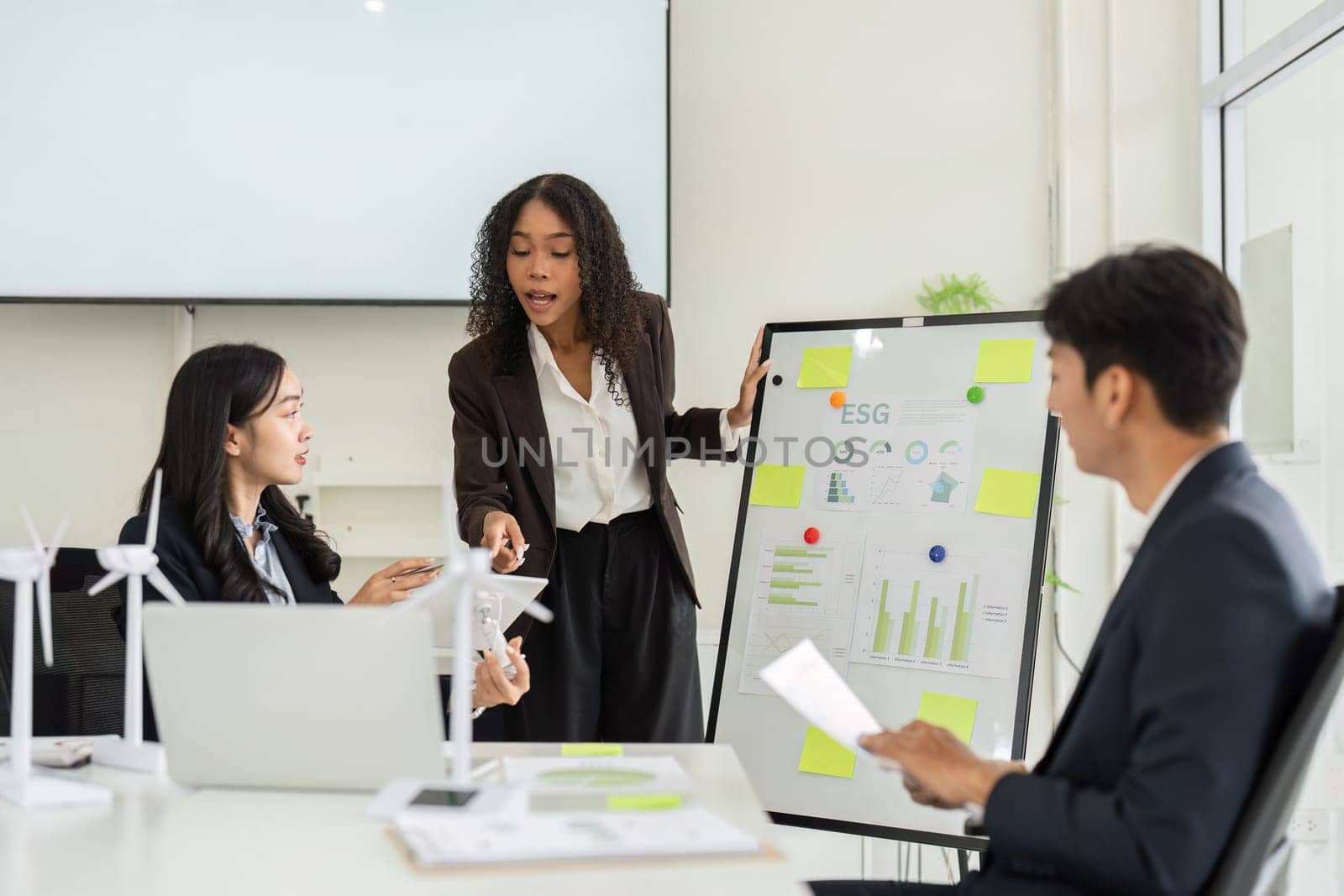 In a modern office, a woman presents key metrics related to ESG initiatives, fostering an open dialogue with her colleagues to drive sustainability efforts.