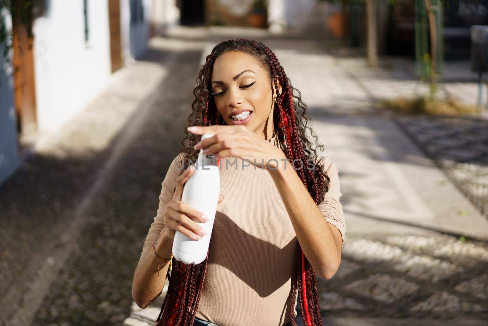 In a vibrant outdoor scene, a young woman with braided hair joyfully holds a refreshing bottle, radiating happiness and confidence, embodying freedom and a spirit of adventure in this perfect moment
