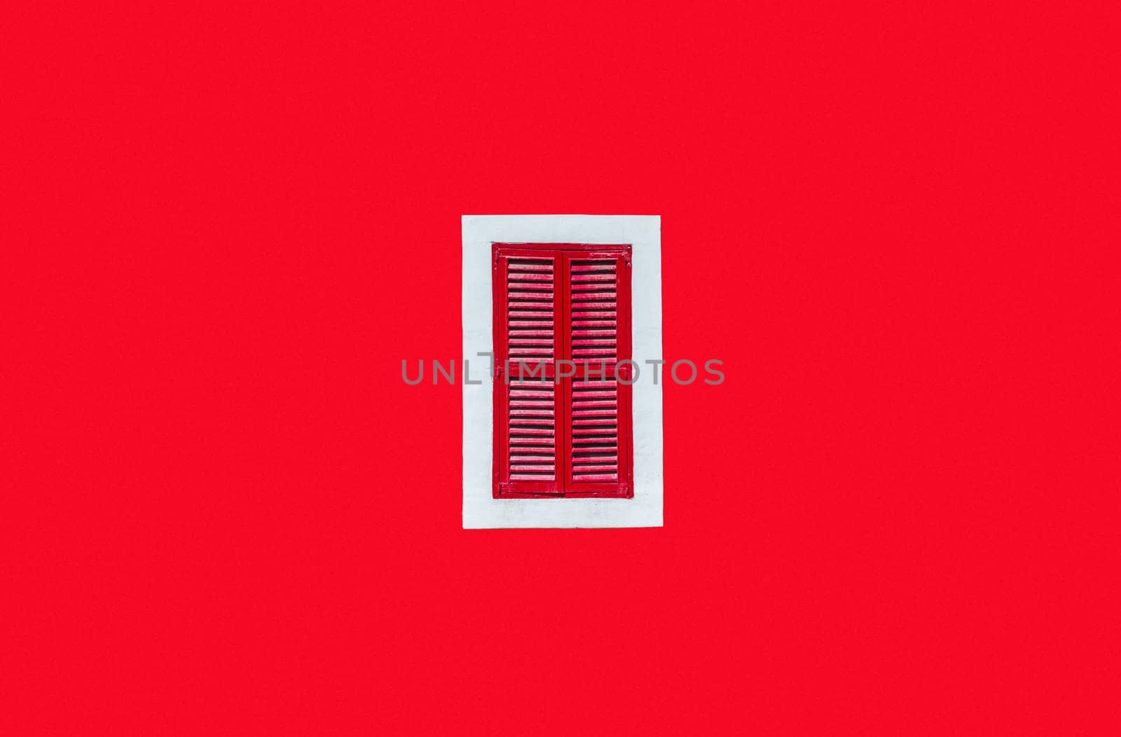 Plain red wall with a red window in a white frame in the middle of the shot