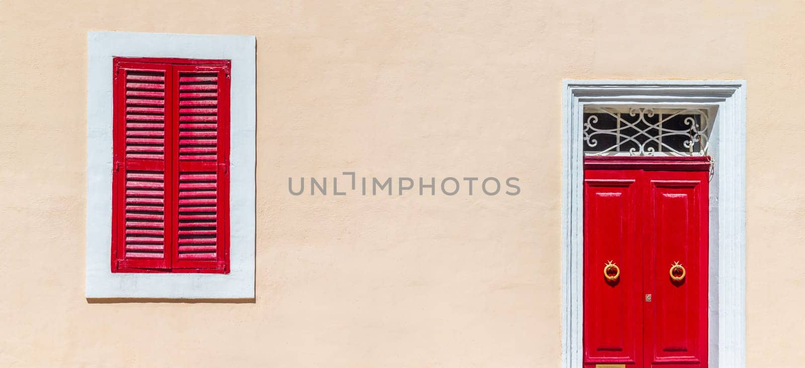 House facade colored in warm beige pastel color with bright red door and shuttered window, wide horizontal composition