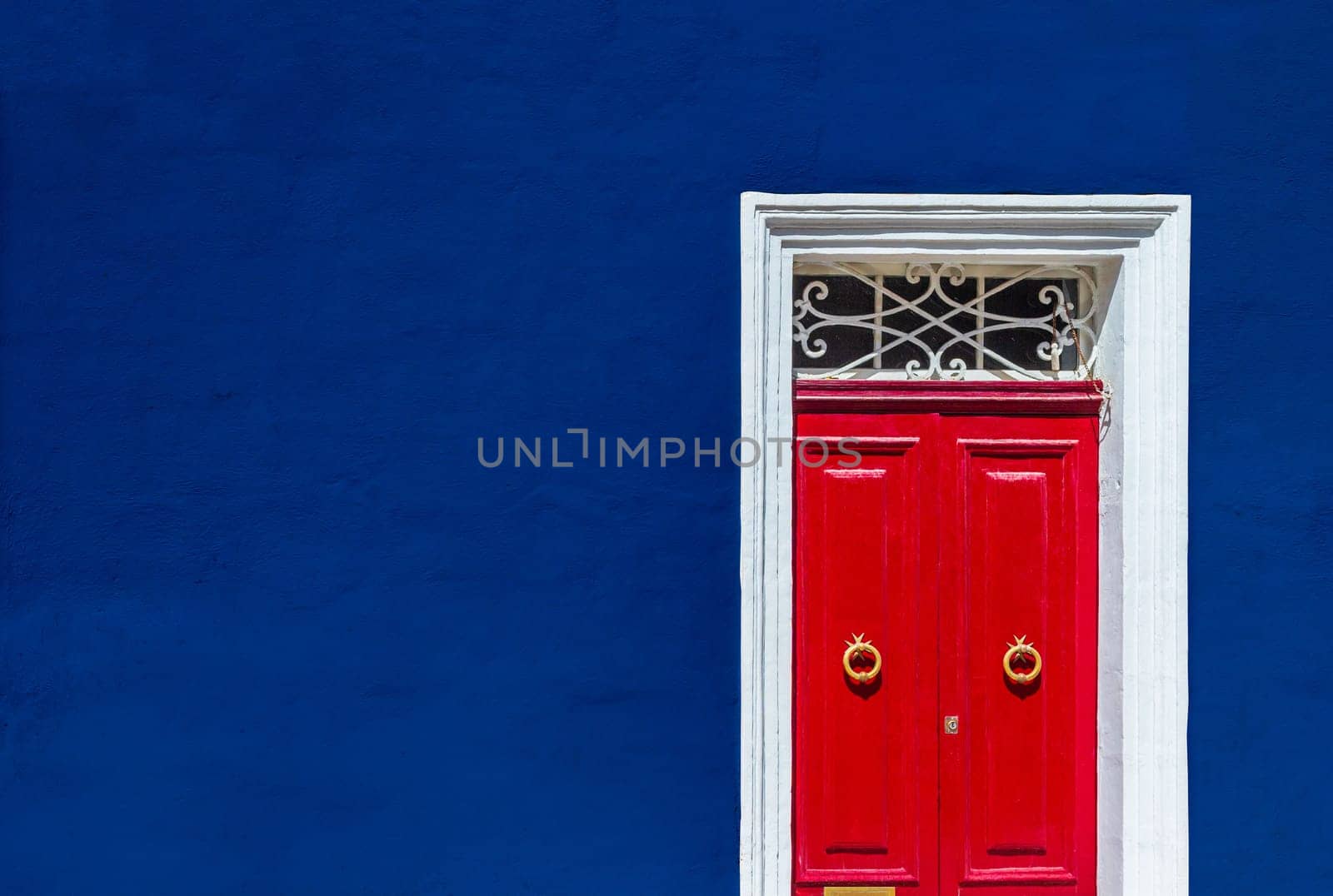 High contrast photograph of dark blue wall of residential building facade with red door in white wooden frame