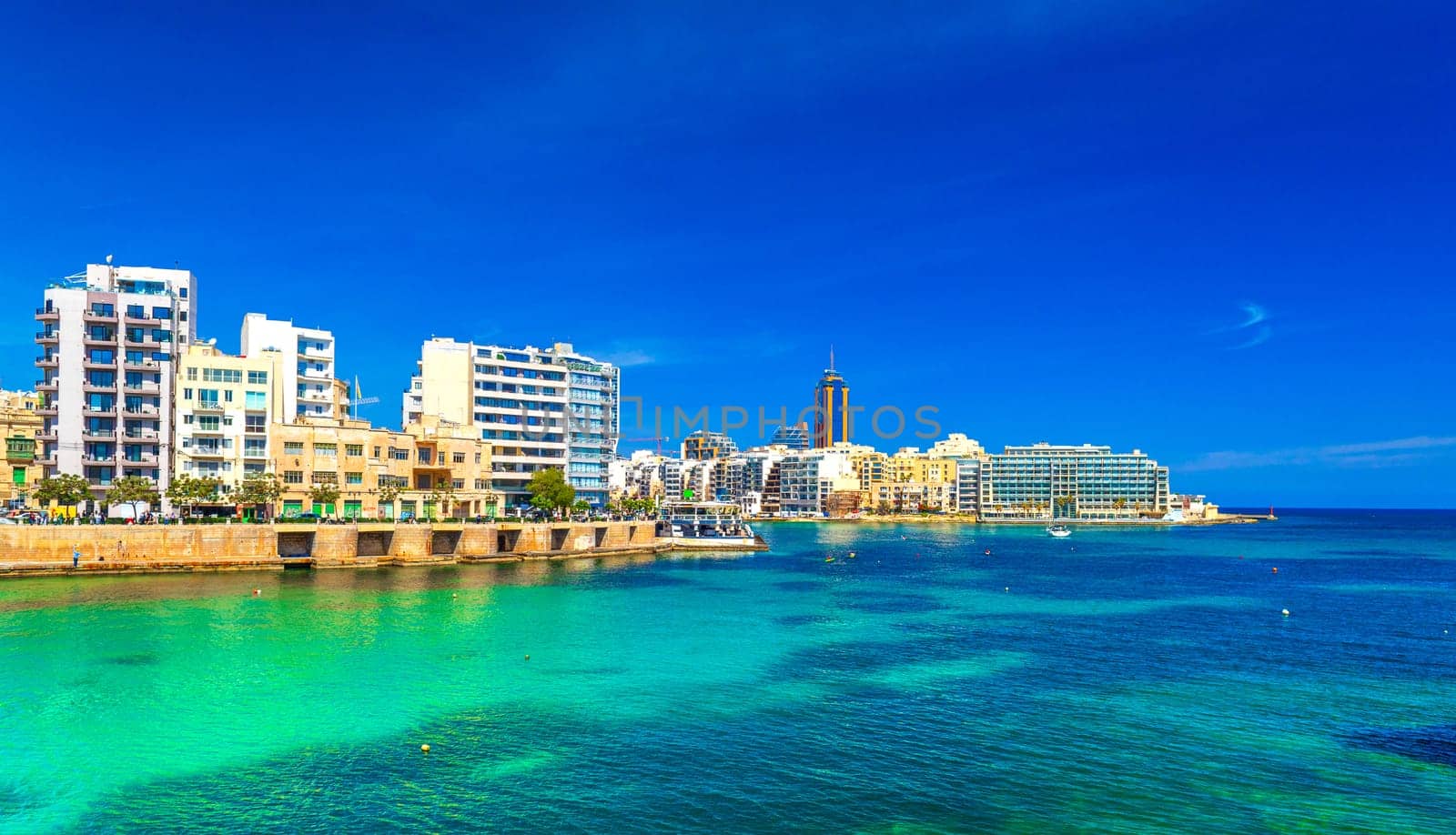 Cityscape of St Julian's Bay on a sunny day with clear blue skies and turquoise water, Malta